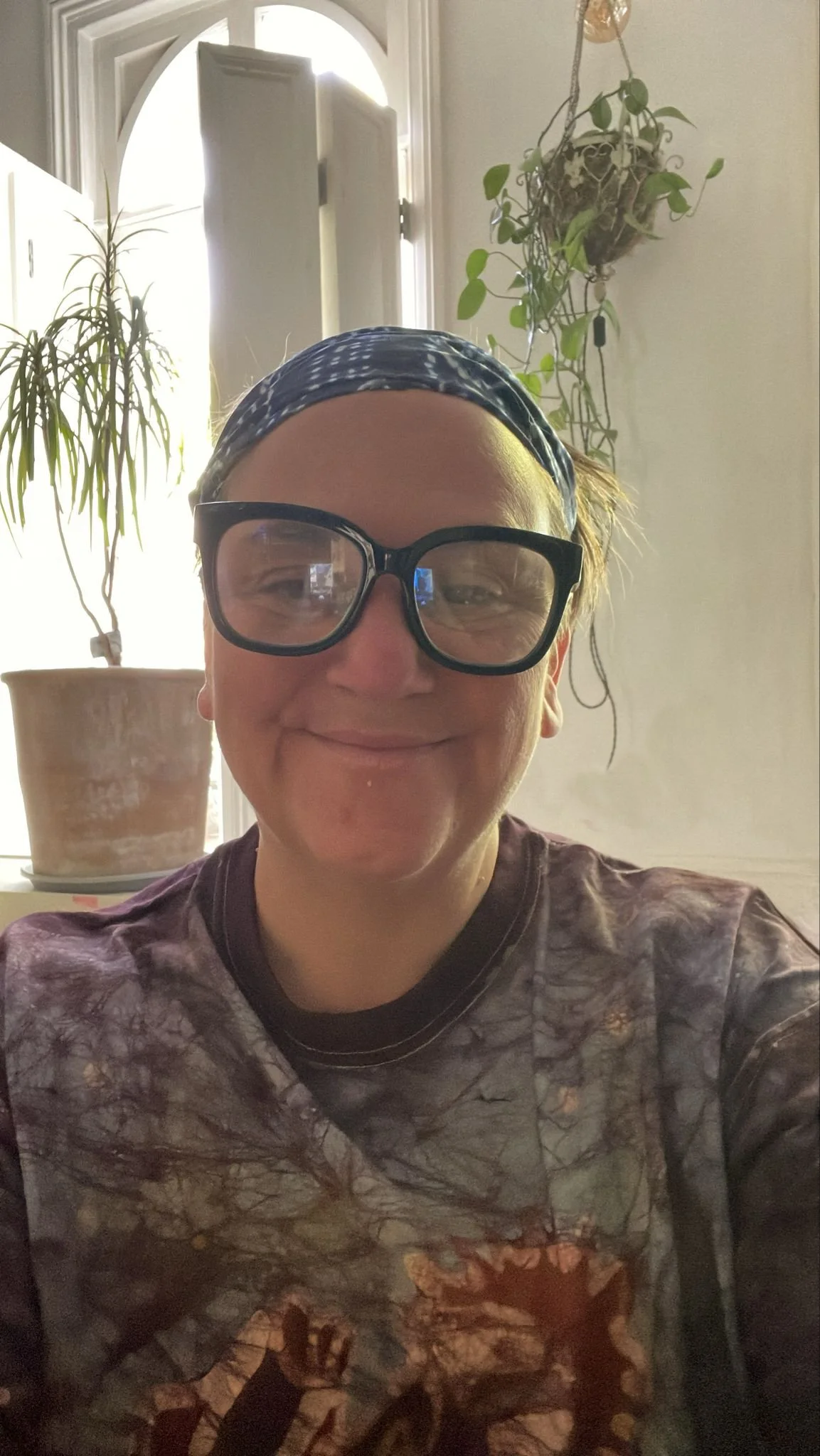 a picture of Janice in a warm purplish tshirt, smiling, with reading glasses and a blue headband