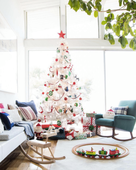 I love the white tree with the more classic colors of Christmas - red and green. It looks great in this sun filled room. Image via Domino and Em Henderson