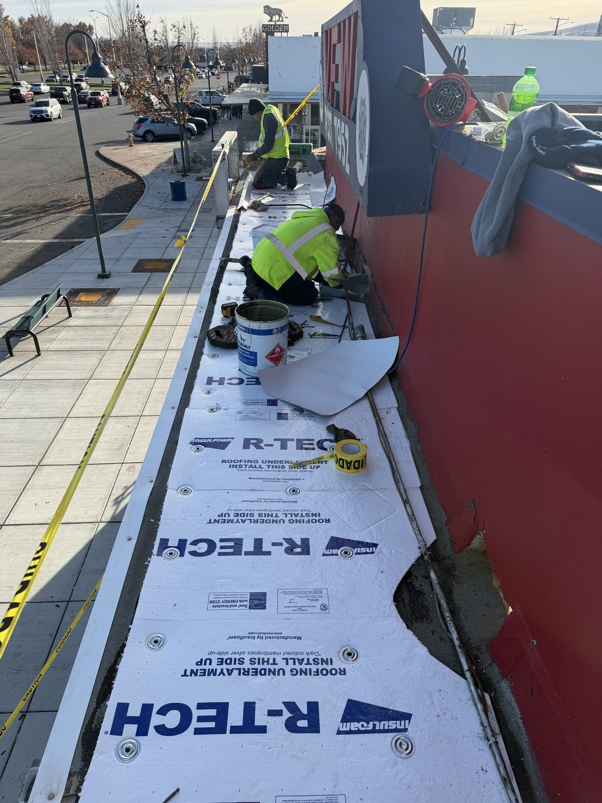 Roofing crew installing insulation board along a parapet wall on a commercial roof in Richland, Washington