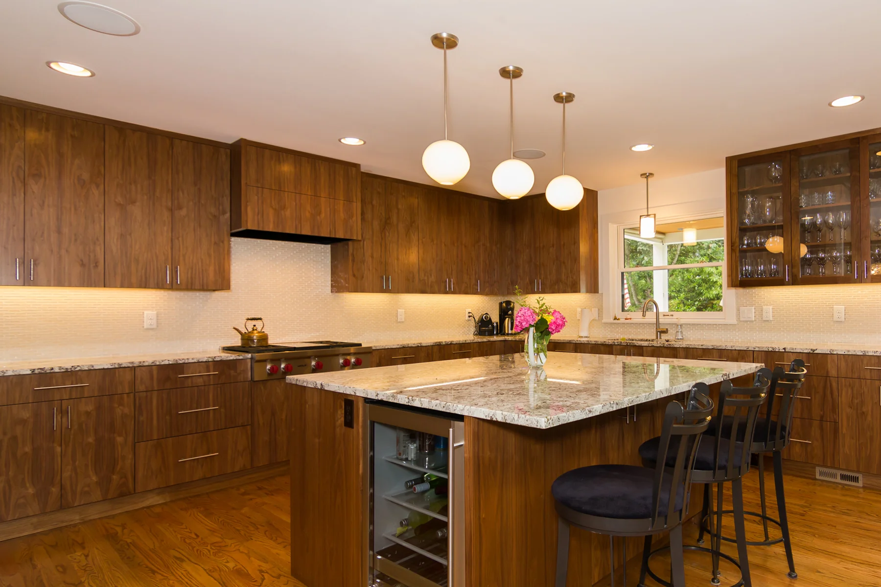 Kitchen detail with custom walnut cabinets, granite countertops, and handmade glass pendants over large island.