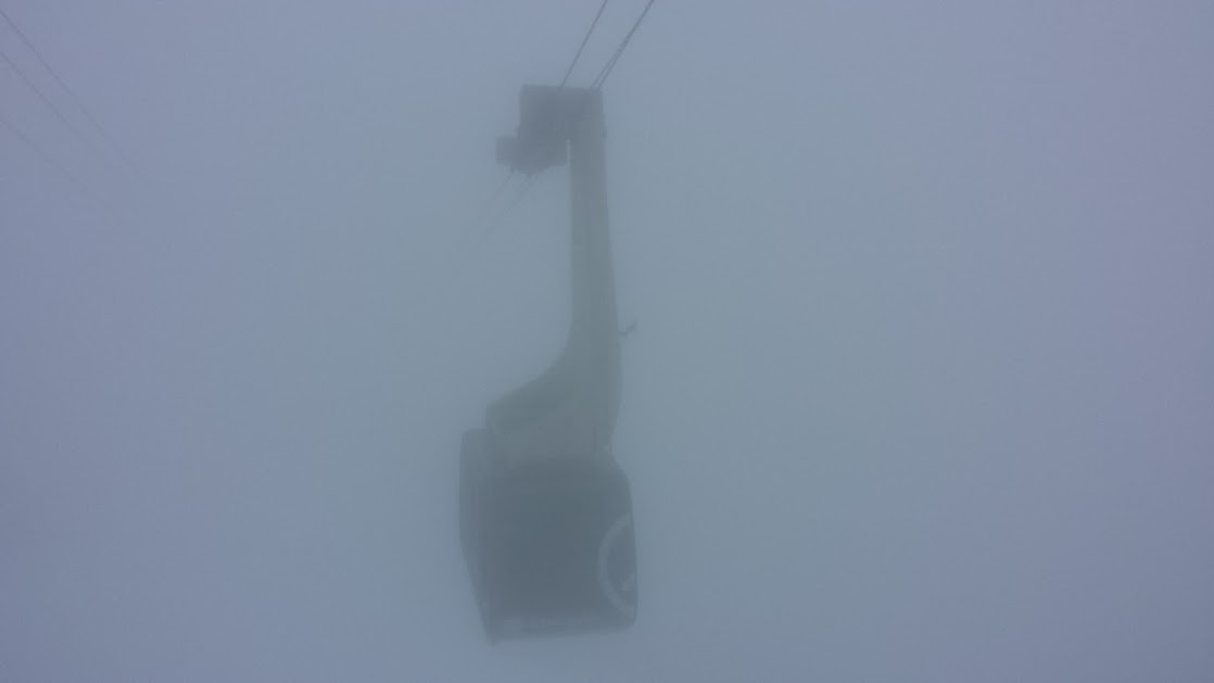 The cable car swimming out of the fog and into the station. 