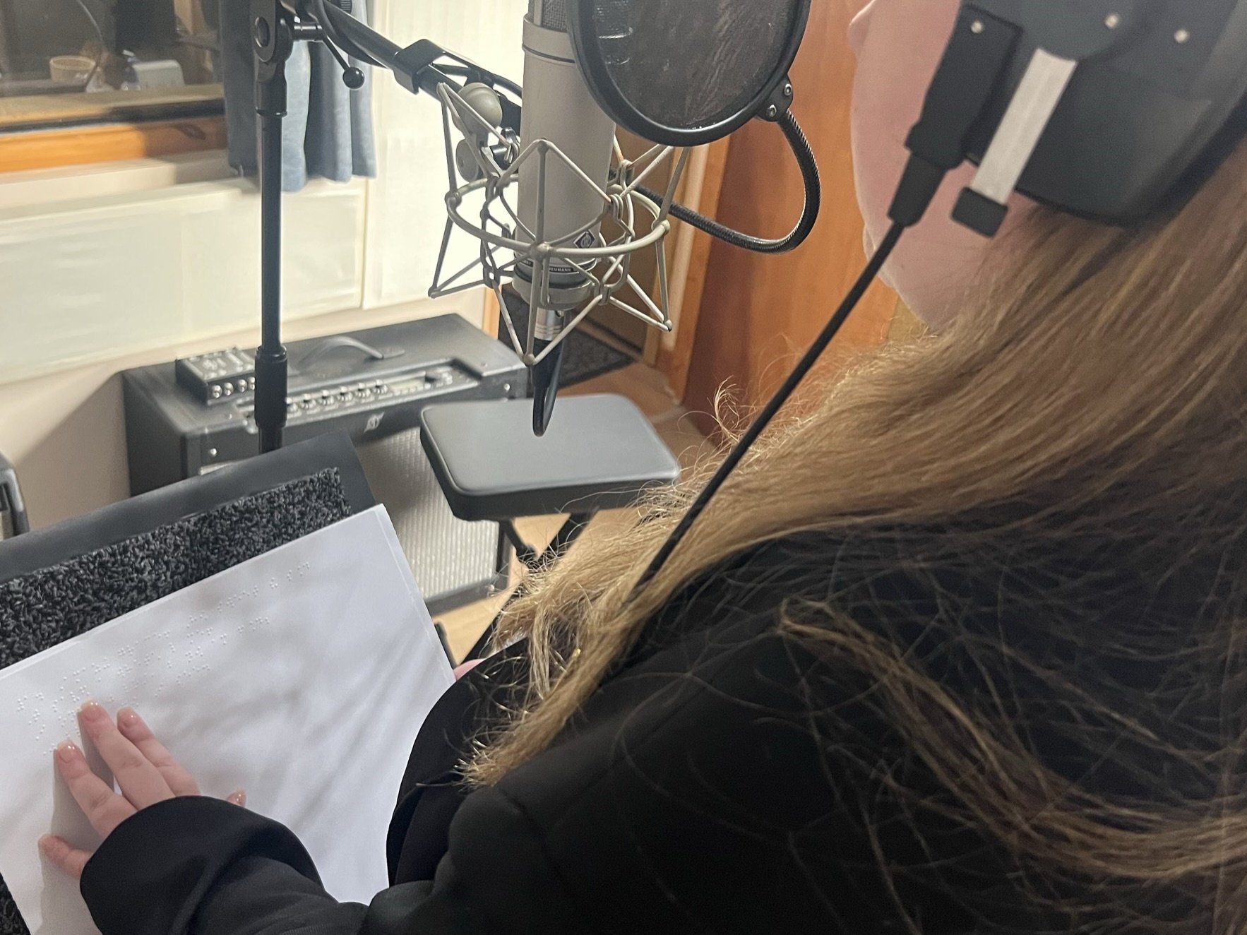 Photo over emily's shoulder in studio reading braille song sheet