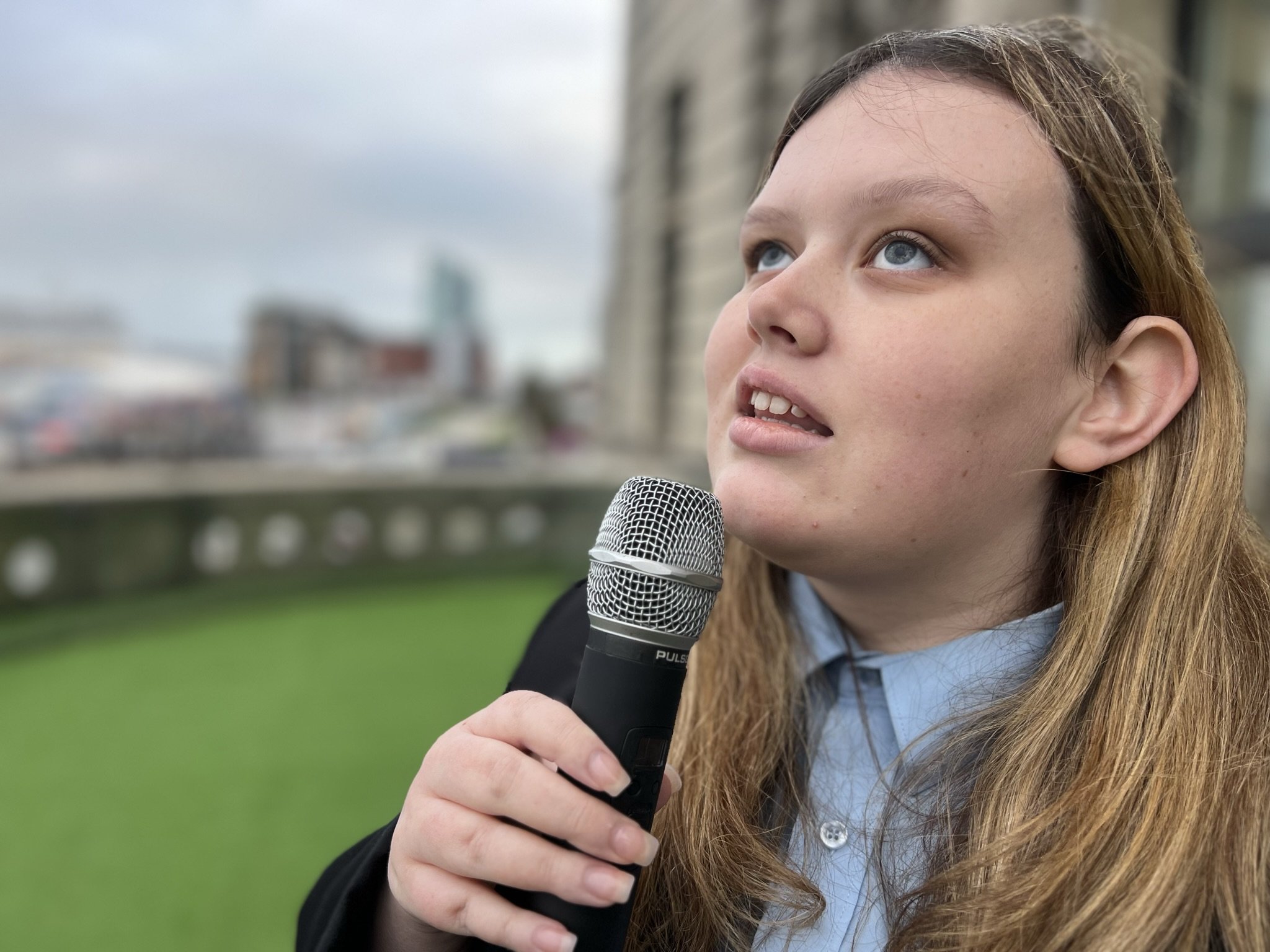 Emily sining holding microphone on balcony at the Liver Building