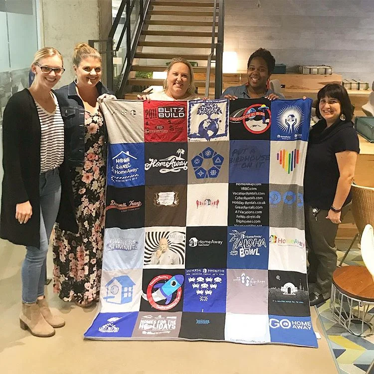 Tiffany (center) showing off her t-shirt quilt made from HomeAway shirts she’s collected during her 11 years with the company.