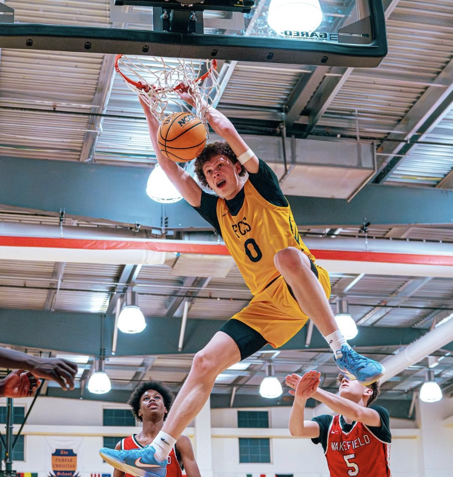 A young basketball player in a yellow jersey, number 0, leaps toward the hoop for a dunk during a game in an indoor gym.