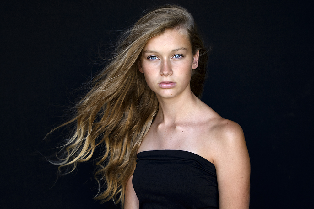 Kleur portret van tiener foto genomen in studio met zwarte achtergrond windmachine en daglicht in Loosdrecht.jpg