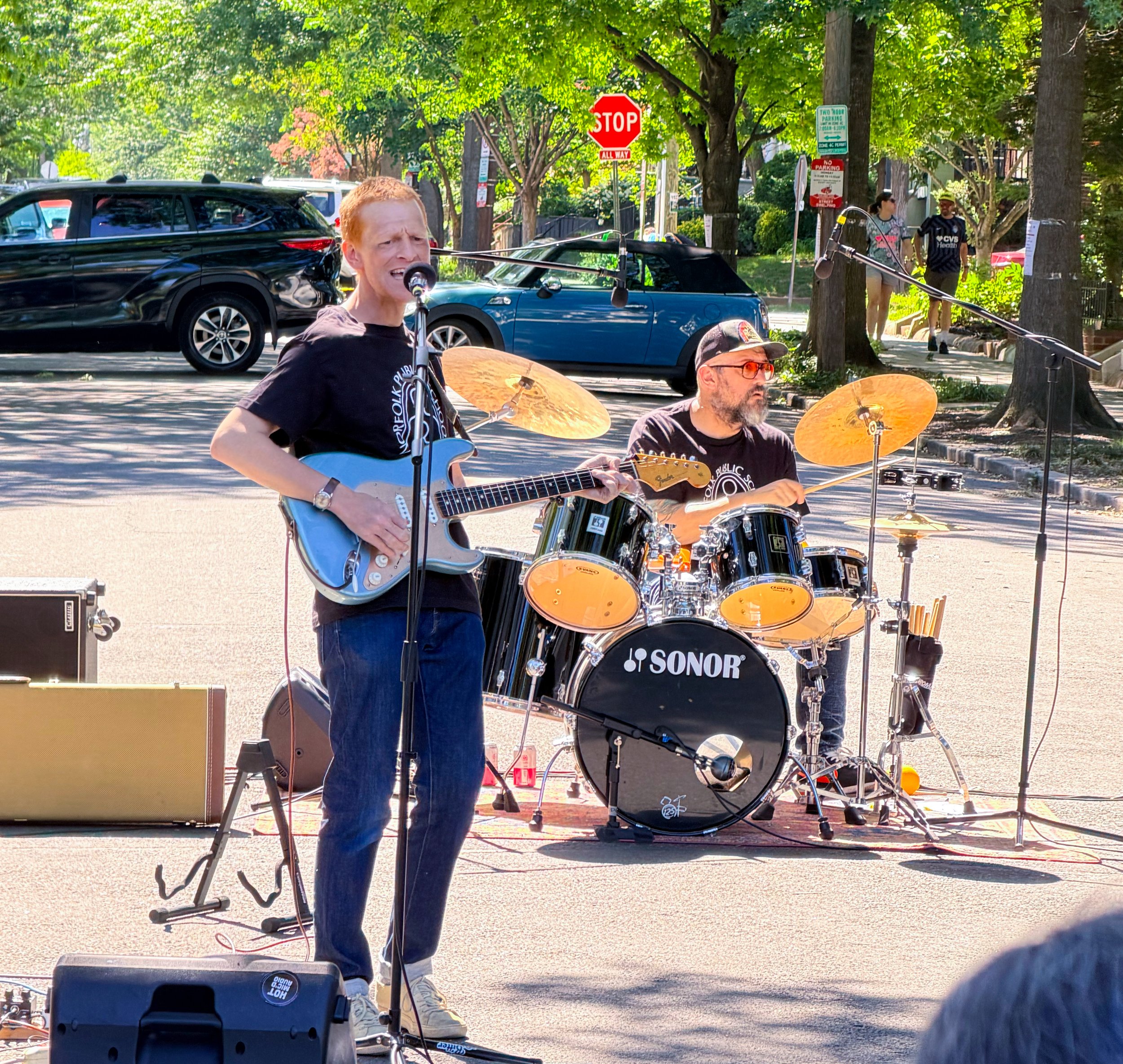 Eric Browne sings and plays blue electric guitar while Jeff Simmermon plays drums outdoors at Petworth PorchFest in Washington, DC.