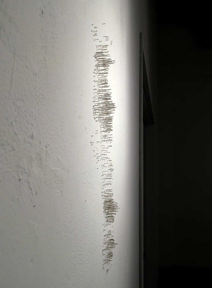 Yucca , 2011 steel pins and latex paint 22" x 8" A mountain-like landscape is created on the wall by mapping the location of each nuclear test that occurred on the flats of the nuclear testing range in Nevada. Each pin is painted to match the wall. Shadows paint the wall.