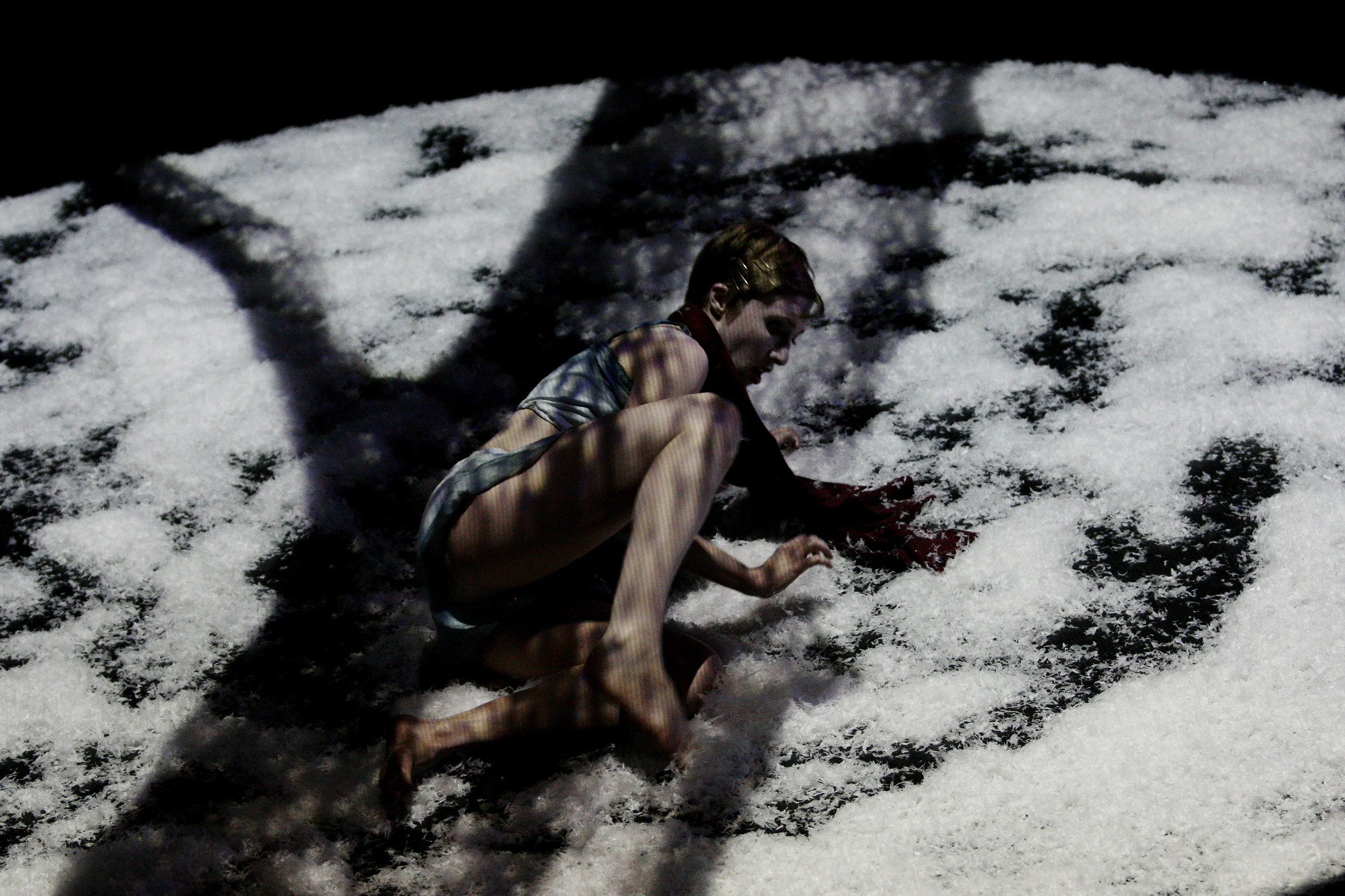 A woman on her hands and knees on snow-covered ground, with shadows cast across her and the snow. From Heather Fairbairn's operatic adaptation of Schubert's Winterreise.