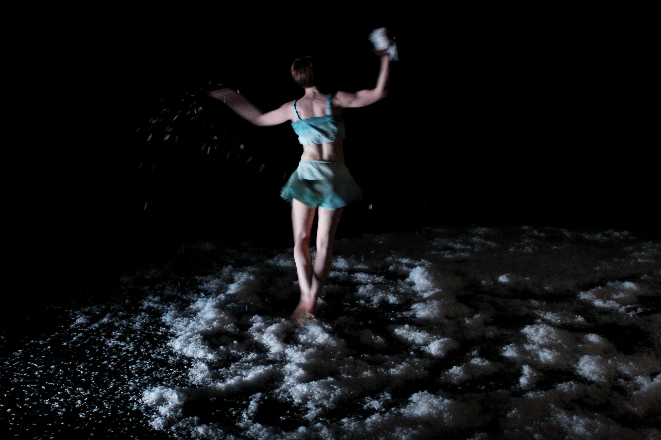 Woman dancing on the beach at night, wearing a blue top and shorts, with water splashing around her. From Heather Fairbairn's operatic adaptation of Schubert's Winterreise.