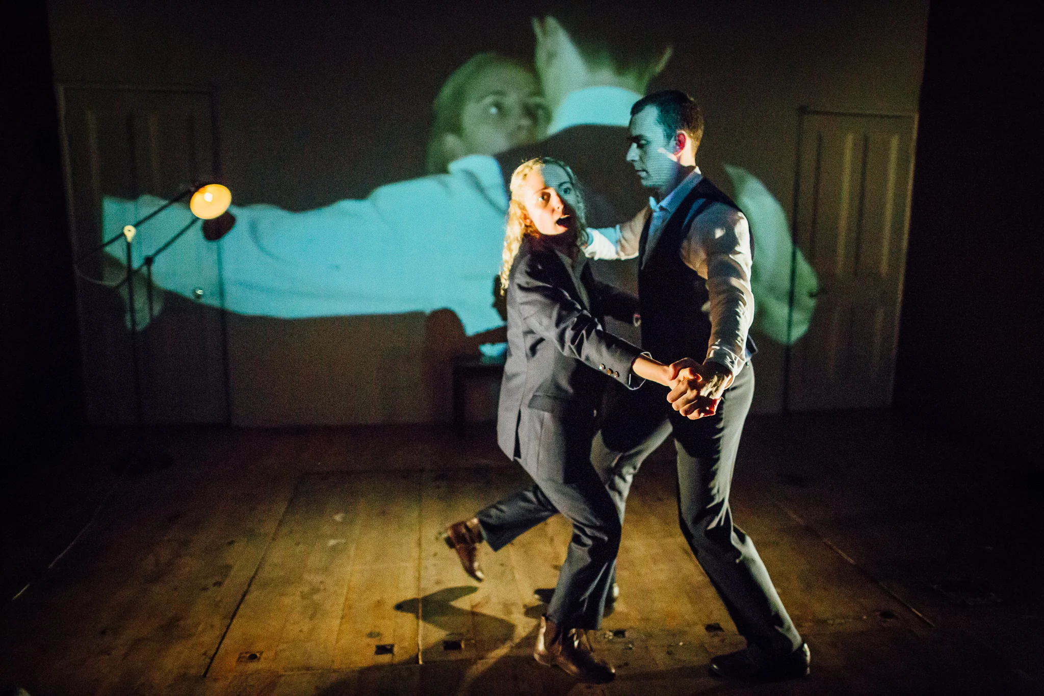 Two people dancing closely on stage, a man and woman, with a projected background showing a face and a person hugging. From The Mutant Man by Christopher Bryant, directed by Heather Fairbairn at The Space Arts Centre, London.