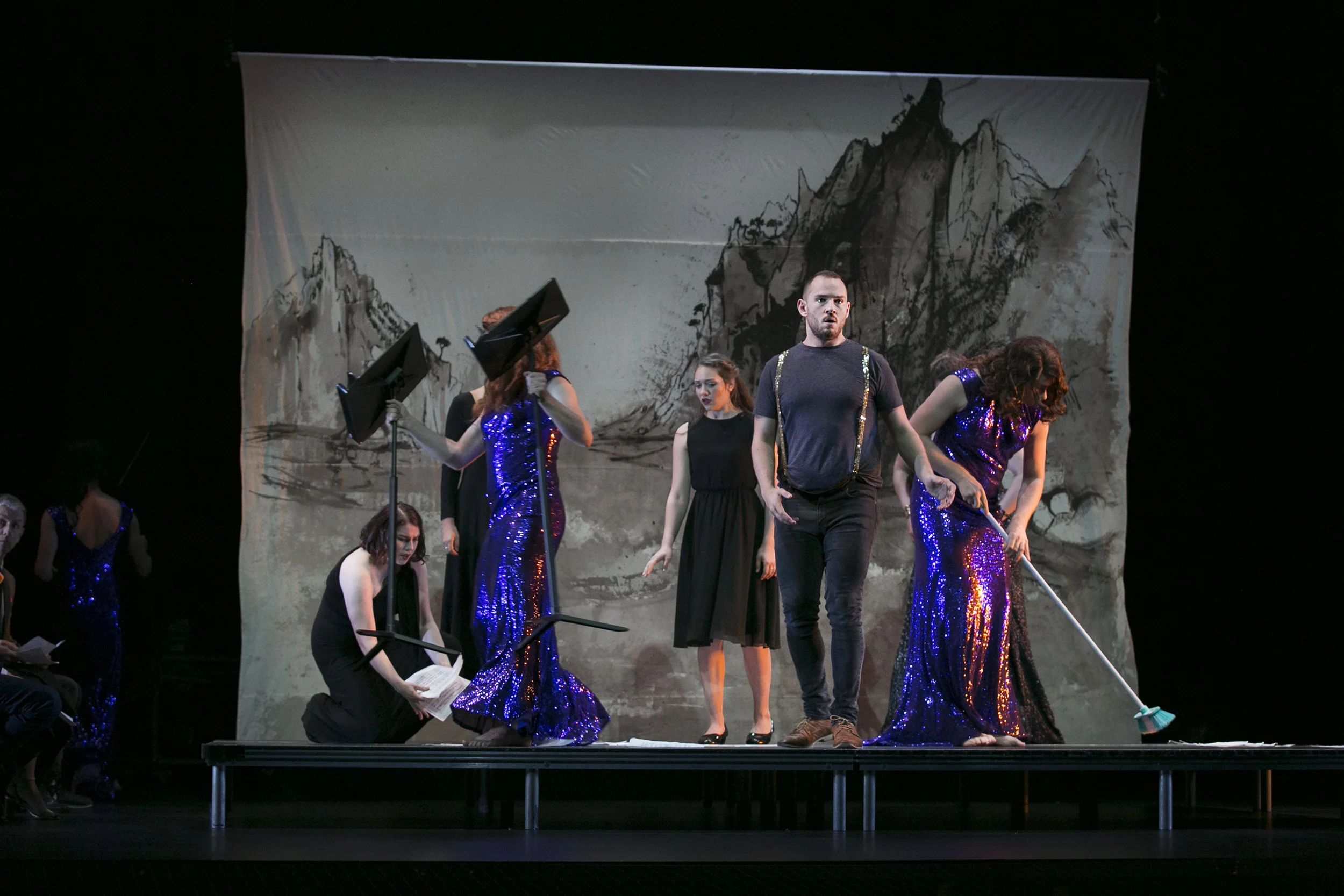 Theater stage with actors in black and sequined dresses performing a play, with a backdrop of mountains. From director Heather Fairbairn's staging of Ariadne auf Naxos at Queensland Conservatorium.
