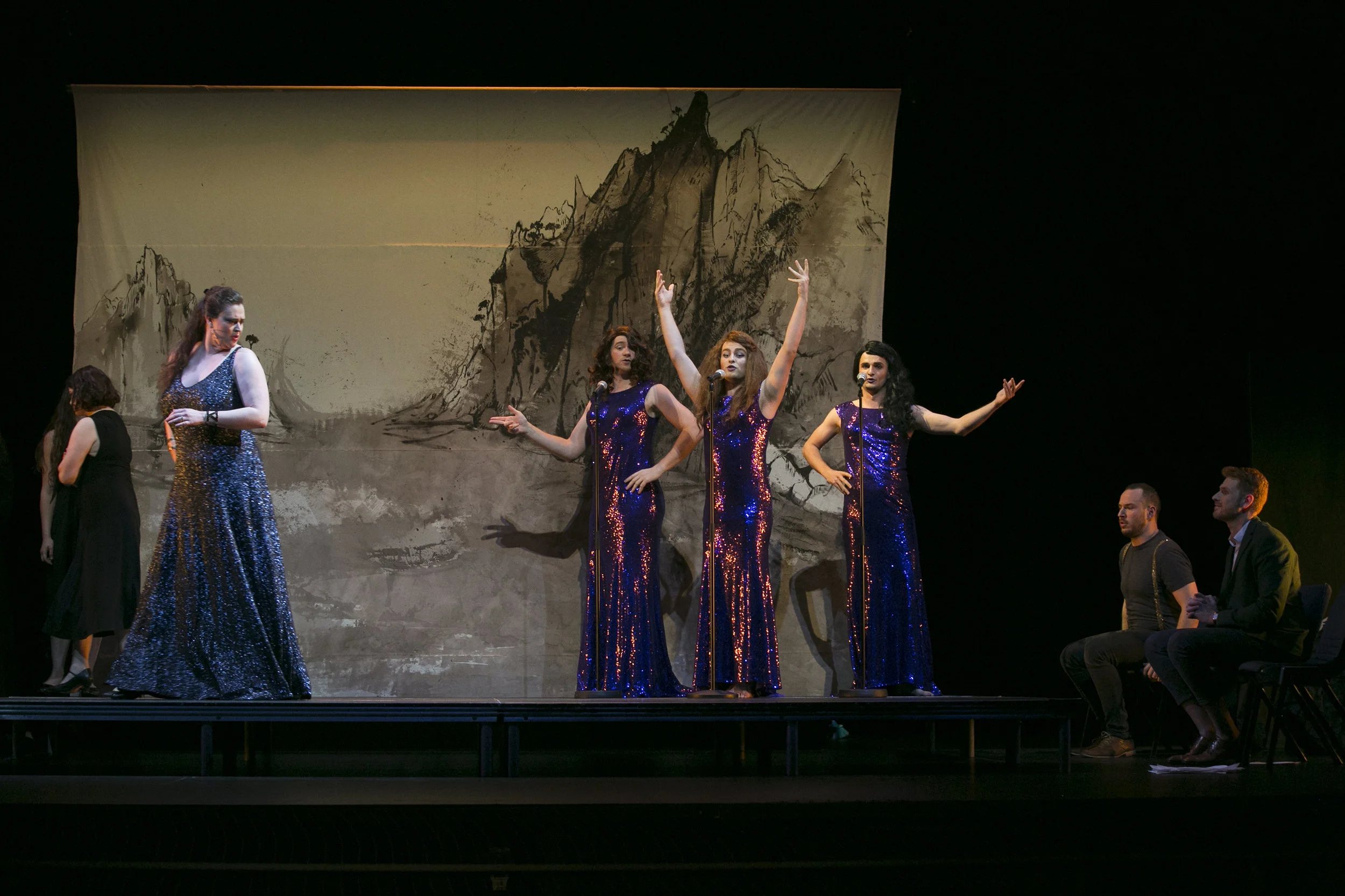 Heather Fairbairn's production of Ariadne auf Naxos. Theater stage with five performers in sparkling dresses, two seated men, and a painted mountain background.