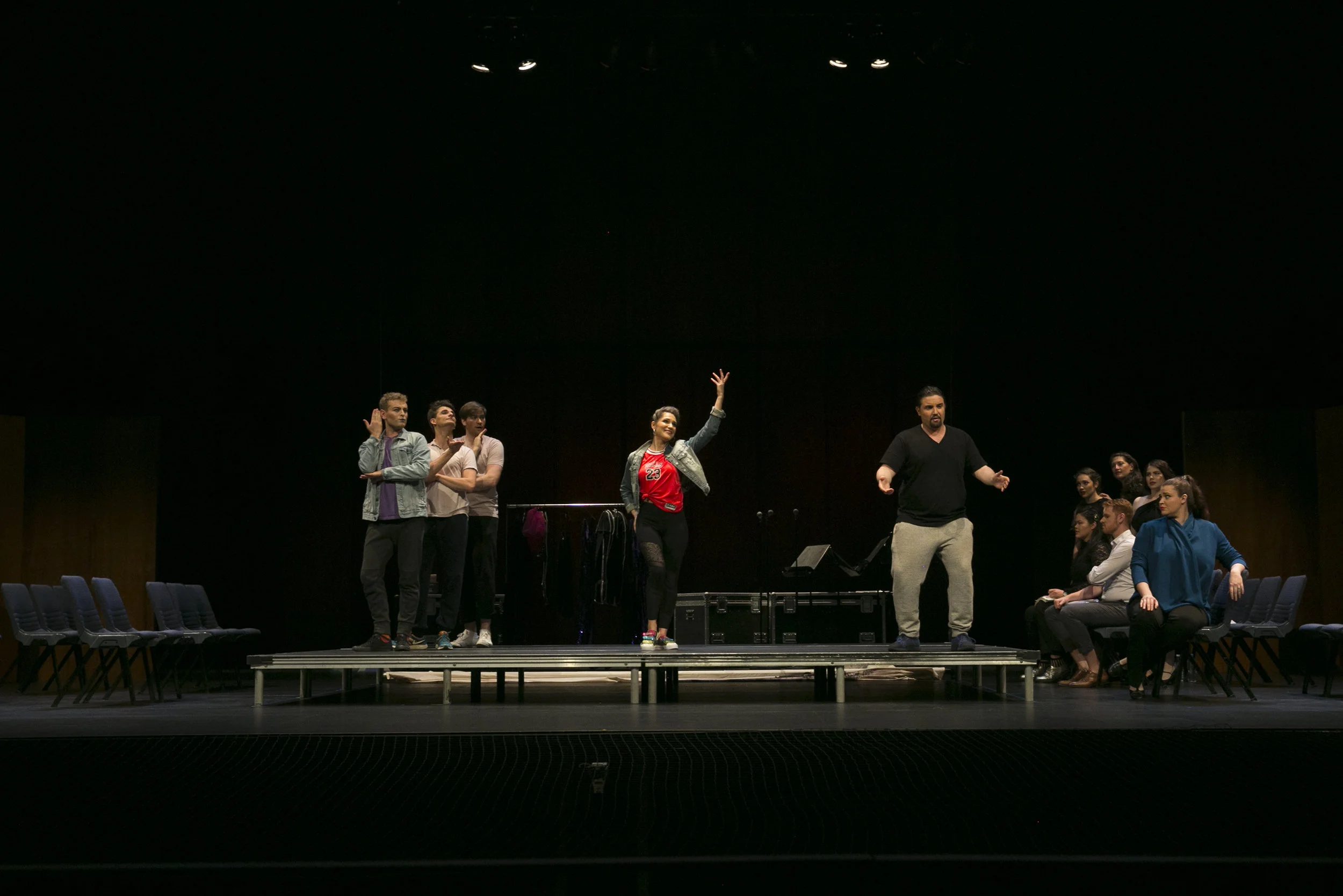Heather Fairbairn's production of Ariadne auf Naxos. Group of people rehearsing or performing on stage, some standing and others sitting, with a woman raising her hand in the center.