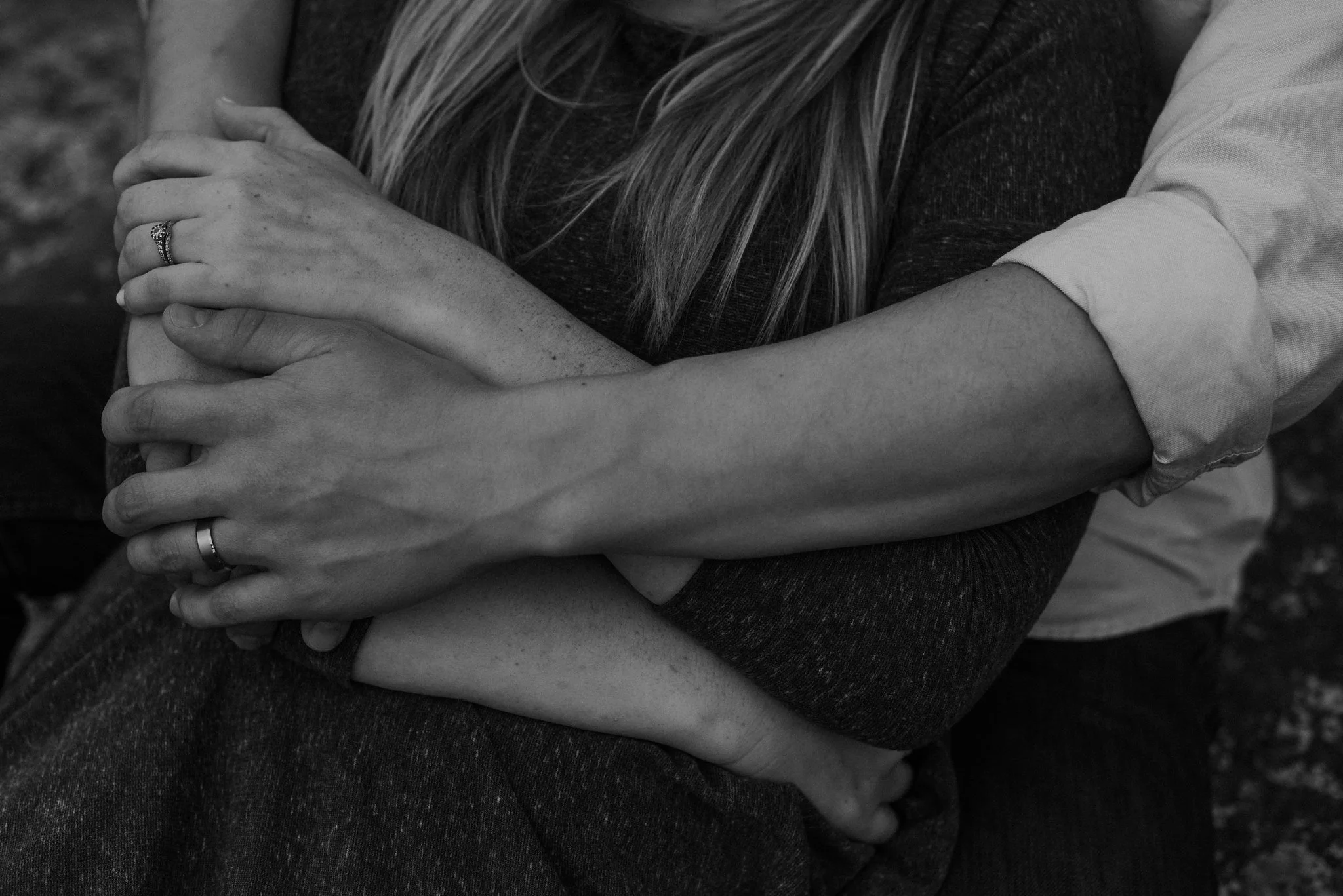Arms intertwined around each other and wedding rings together.