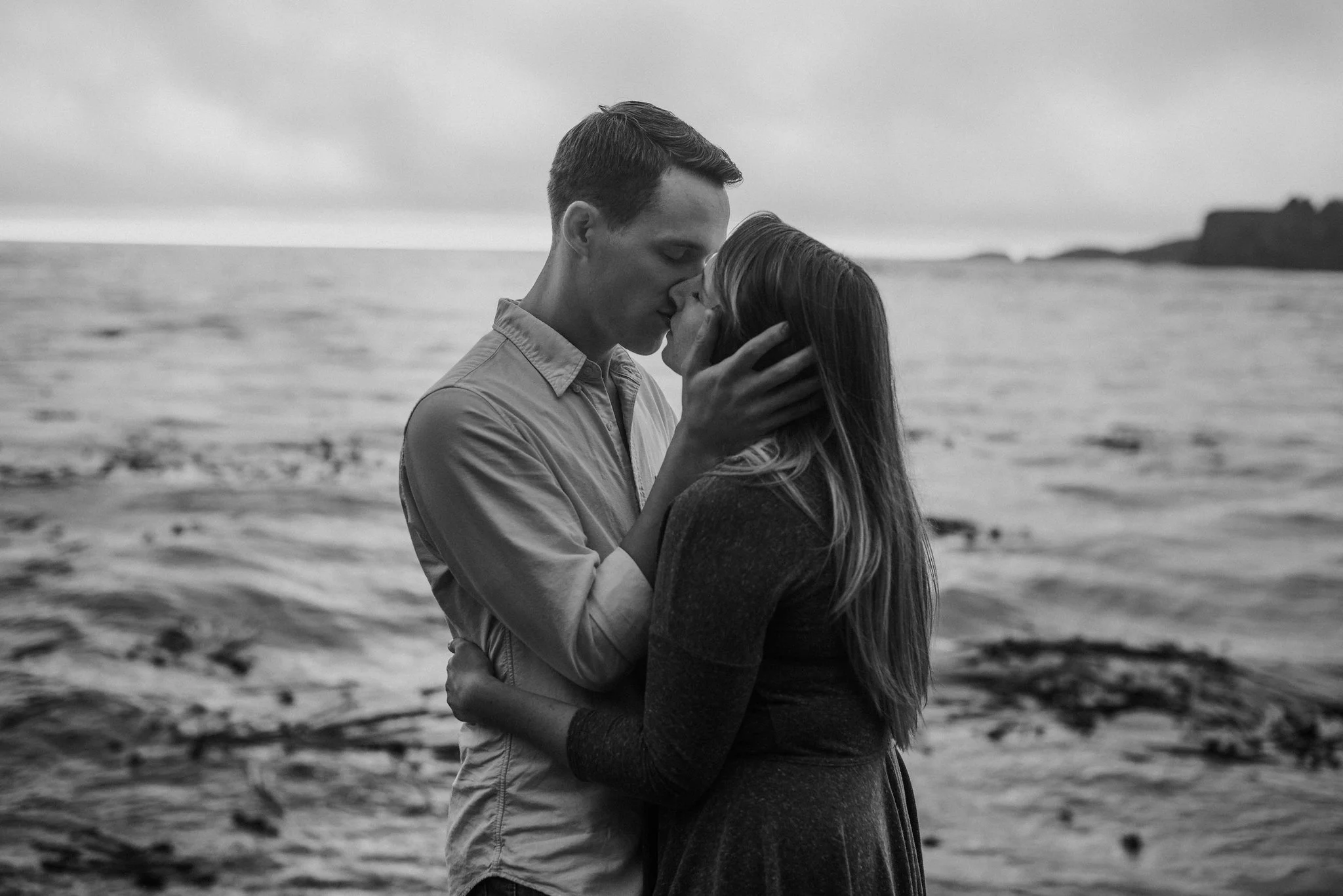 Husband pulling in wife for a kiss at ocean.