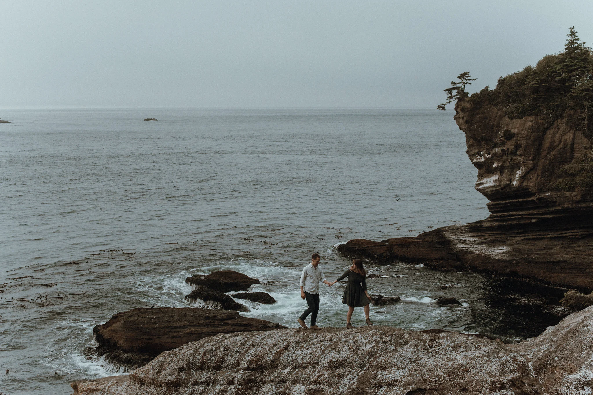 Couple holding hands and walking across rocks at ocean rocky coast.