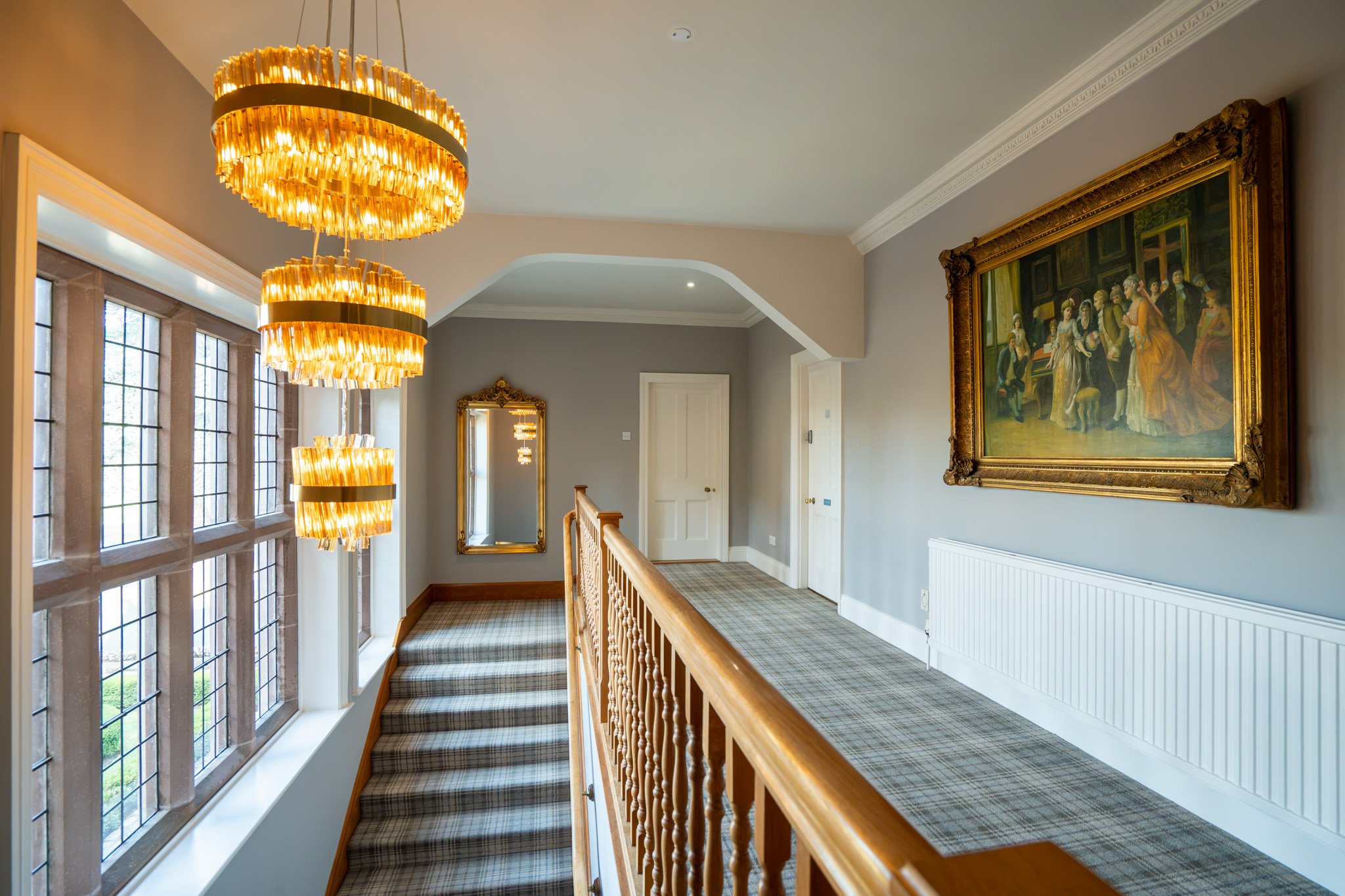 Interior of a house with a staircase, large stained glass window, framed painting, and gold chandelier