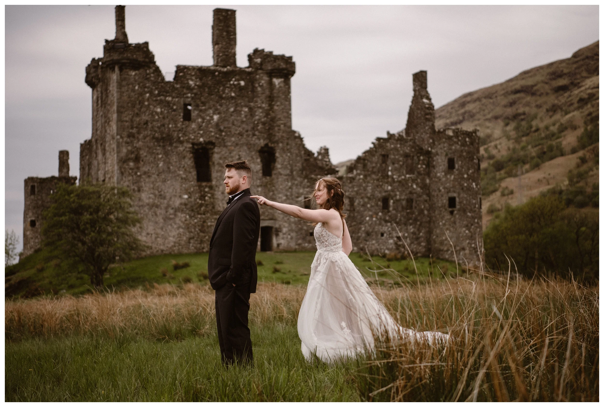 The ruins of Kilchurn Castle in Lochawe in the Scottish Highlands are behind Elissa and Daniel during their first look before their destination elopement. Photo by Maddie Mae, Adventure Instead.