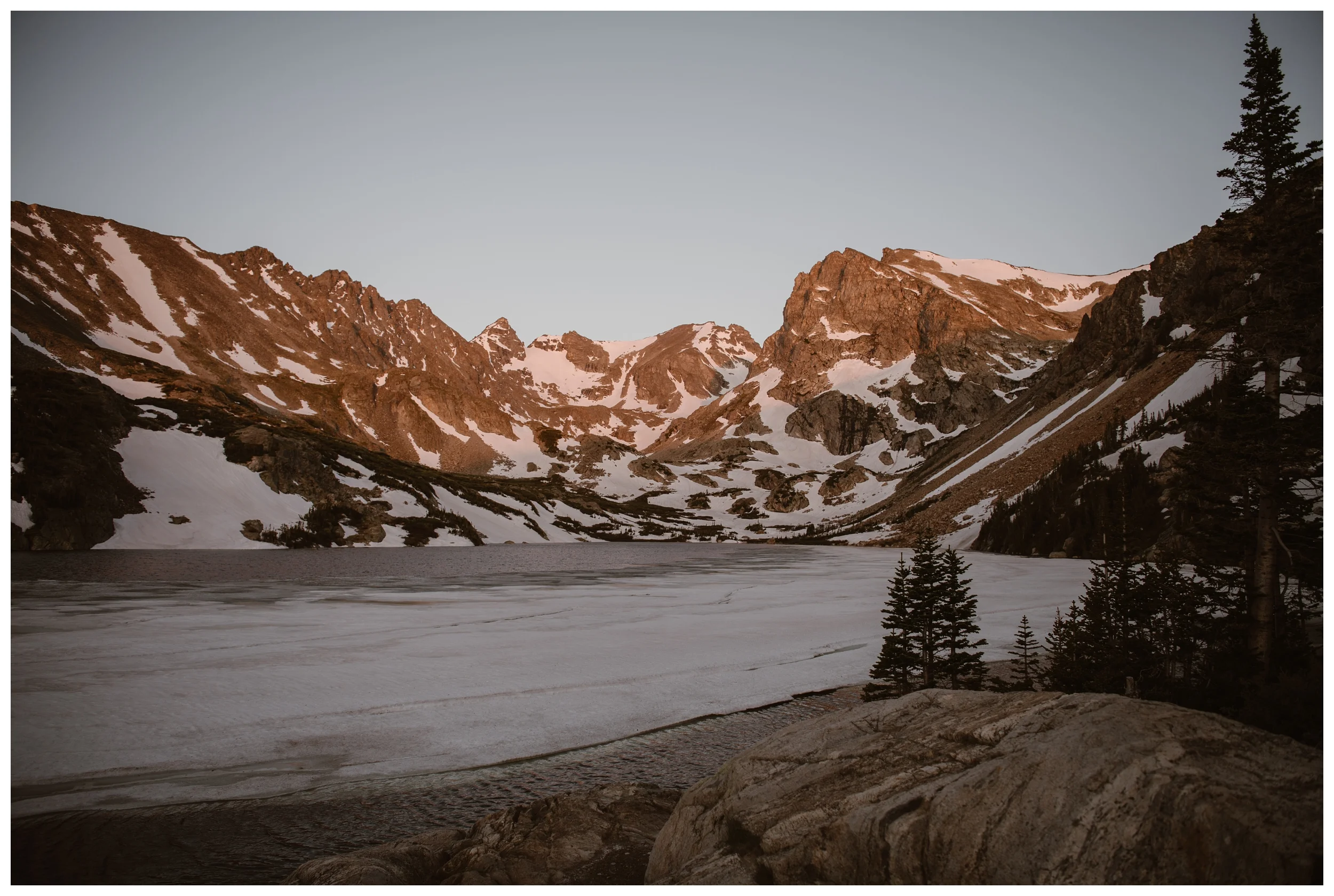 The mountains above Lake Isabelle glow before dawn. Alpenglow makes mountains glow pink, which is a beautiful backdrop for an adventure hiking elopement. Photo by Adventure Instead, Maddie Mae.