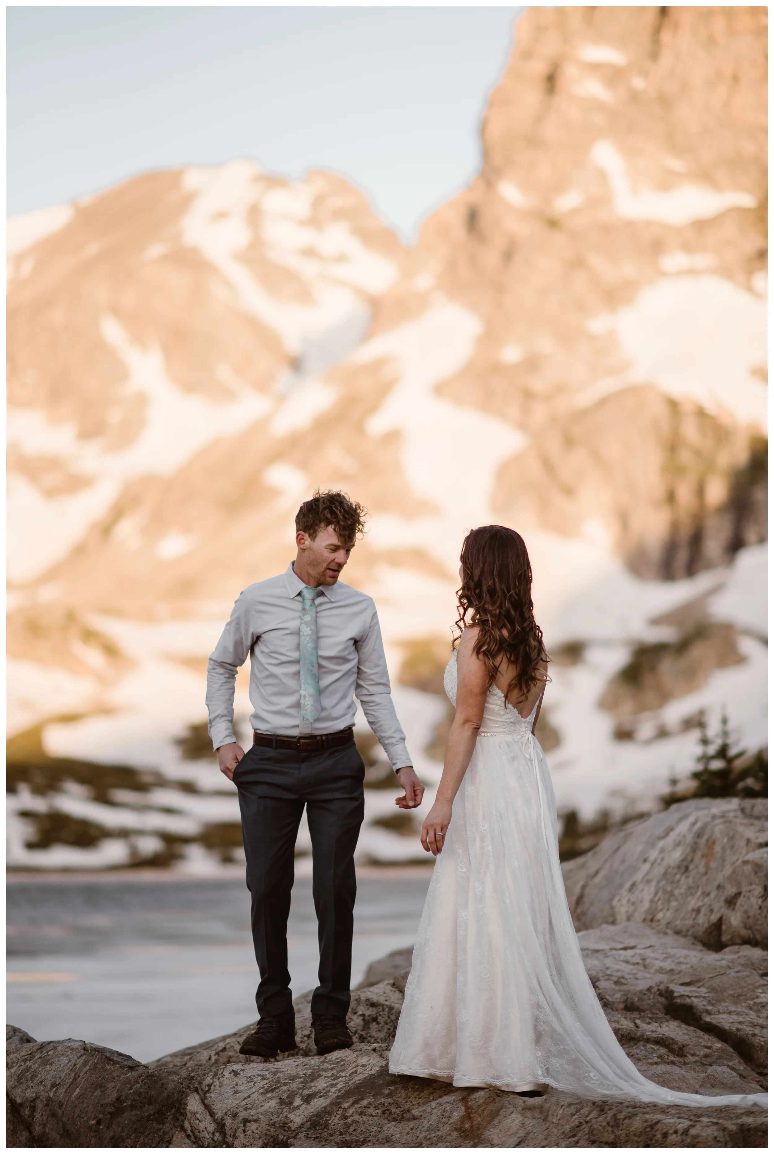 Matt and Karen’s first look for their adventure hiking elopement outside Nederland, Colorado was beautiful with mountains glowing pink with alpenglow behind them. Photo by Adventure Instead, Maddie Mae.