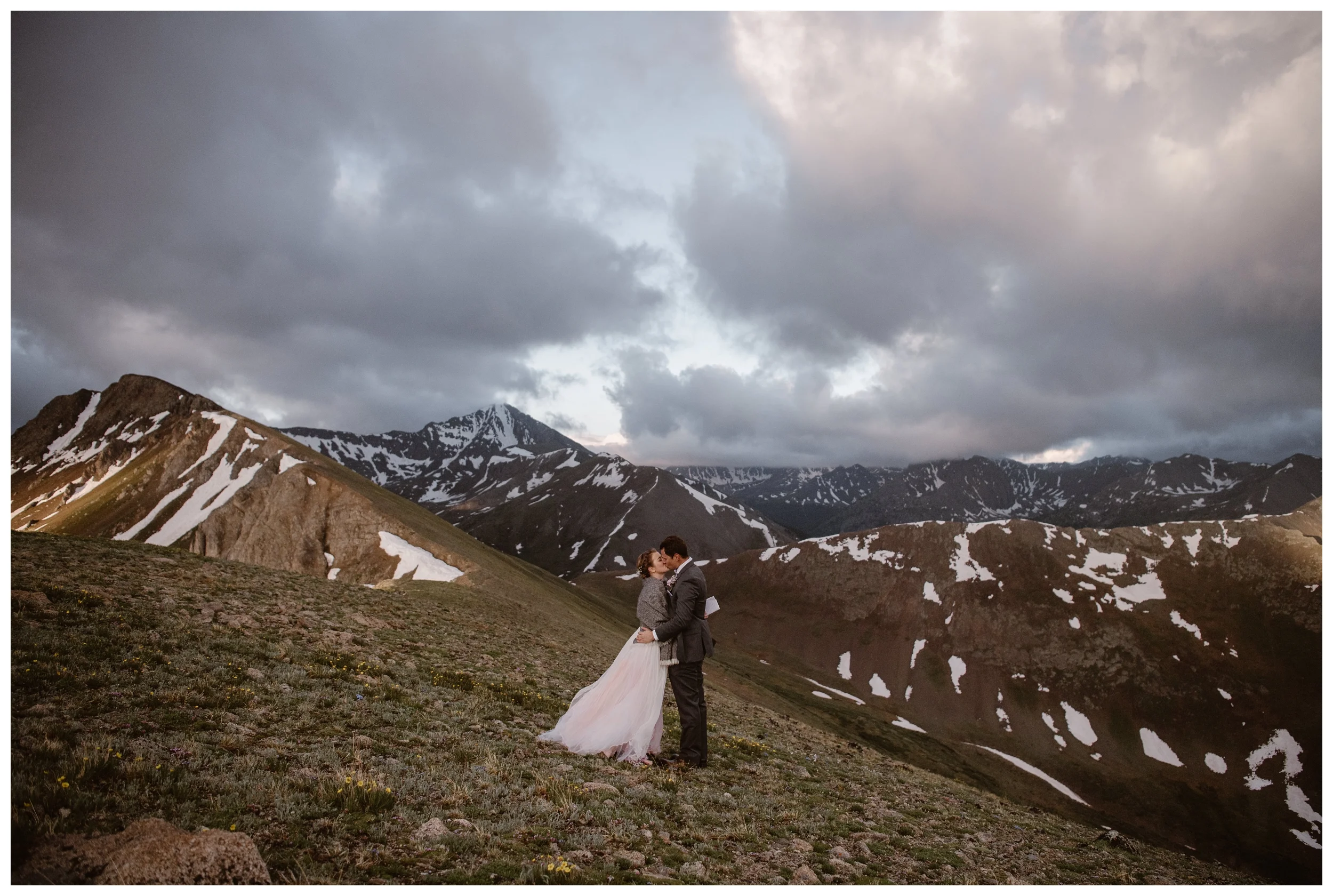 With the jagged mountains of the Sawatch Range glowing pink around them, Marcela and Vasily share their first kiss after their intimate self solemnizing elopement ceremony. Photo by Maddie Mae, Adventure Instead.