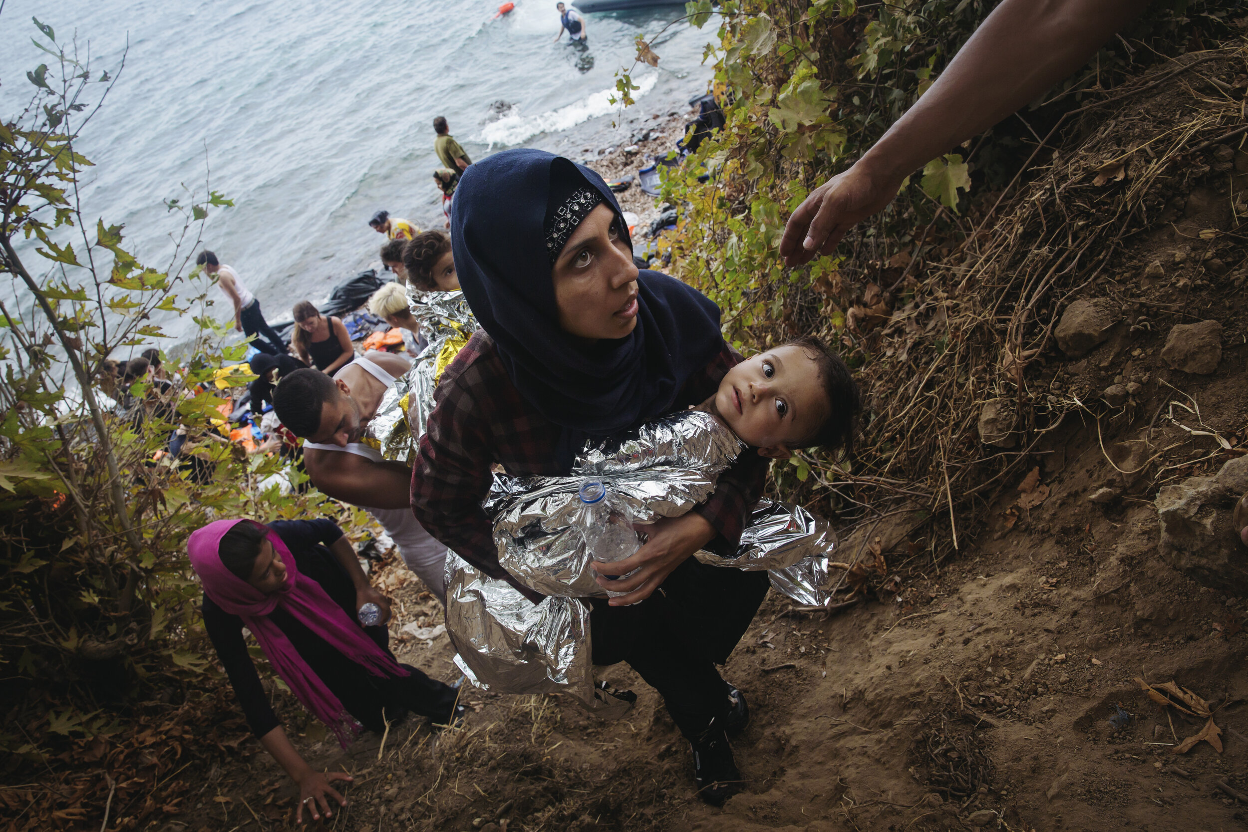   A woman climbs a hill with her baby after coming ashore from Turkey onto Lesvos, Greece during a mass exodus from Syria. 2015  