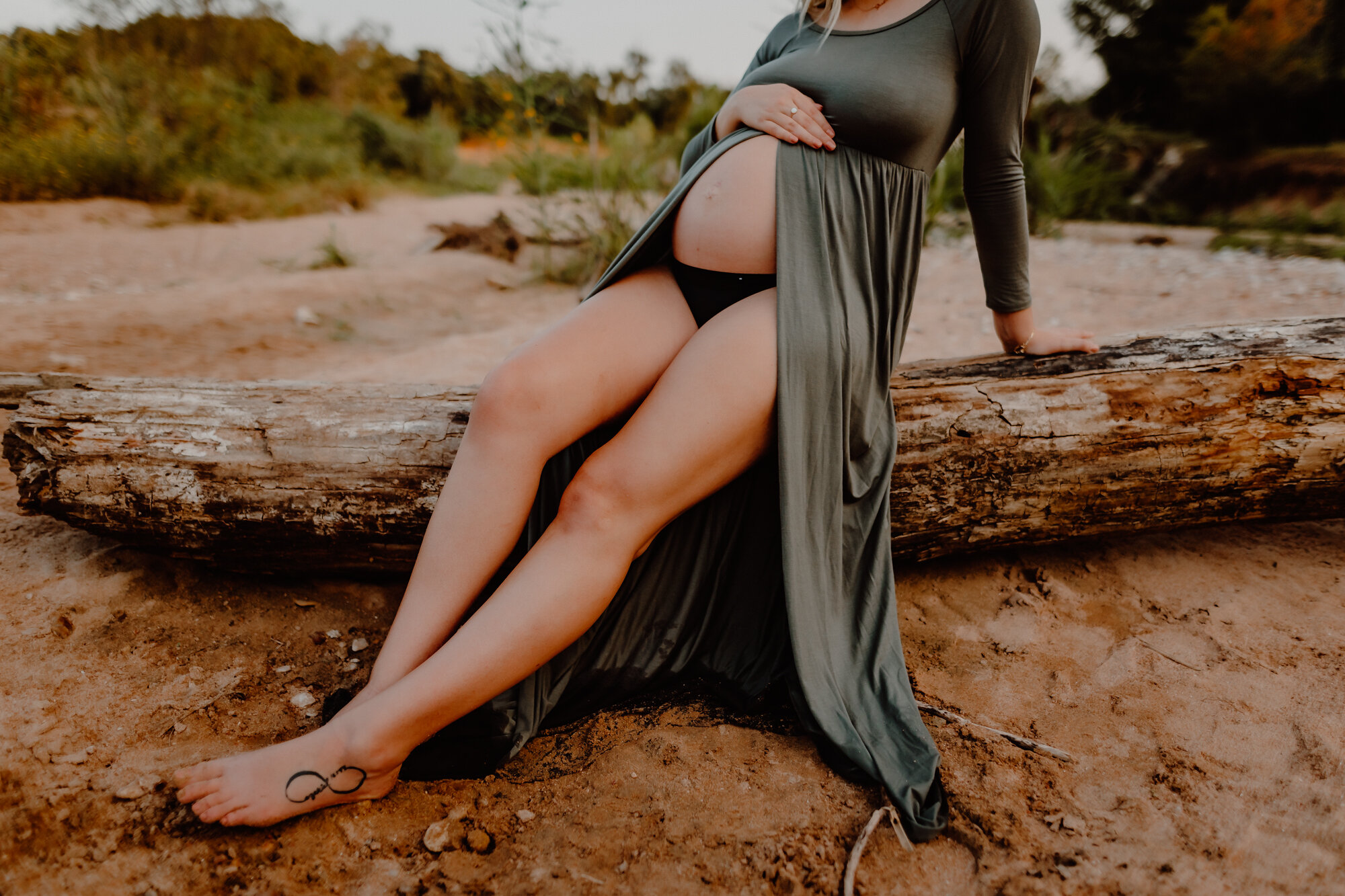 pregnant woman sitting on log in the sand