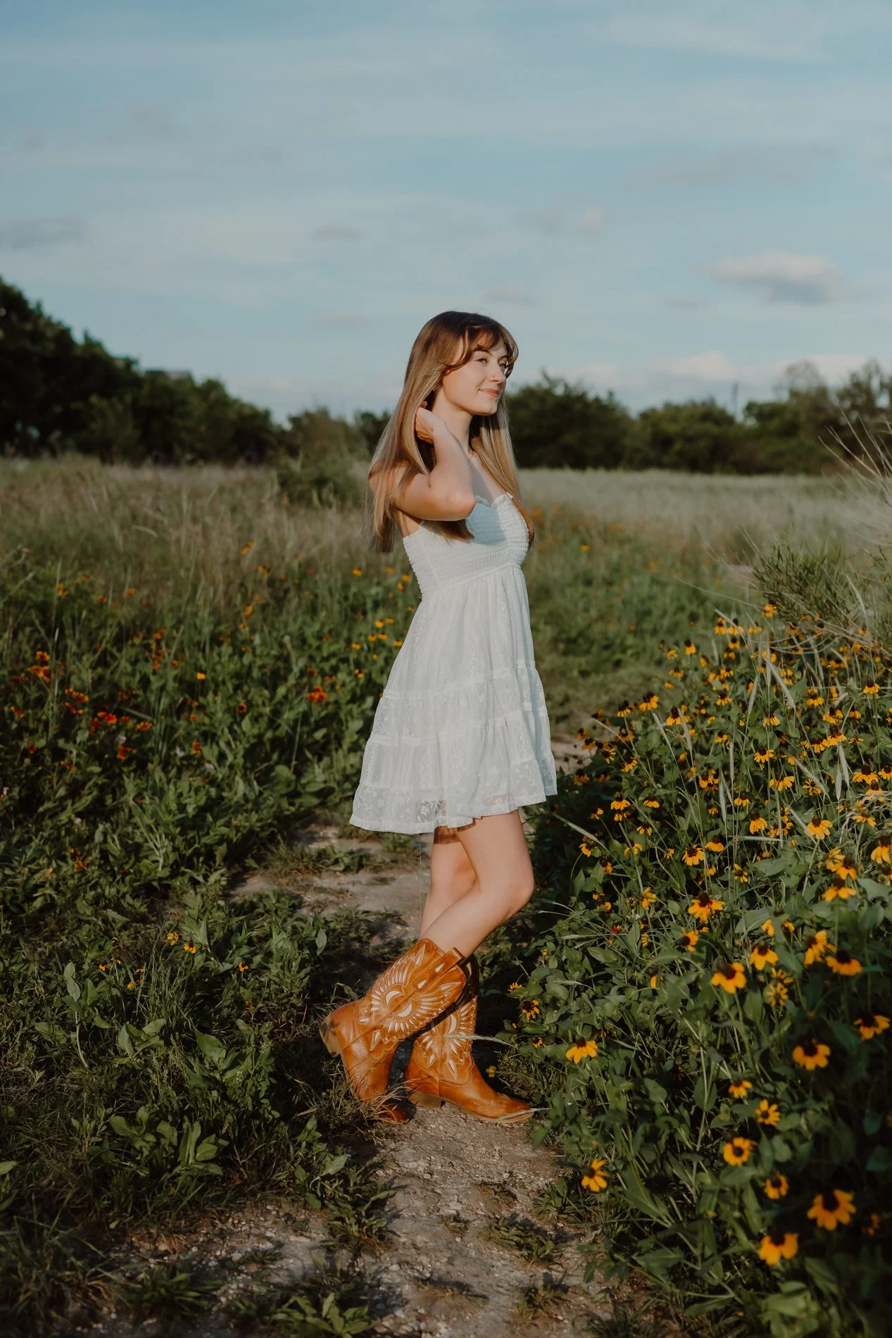 Full-length senior portrait of Dylann in a flowy dress, standing in tall Texas wildflowers near Austin.
