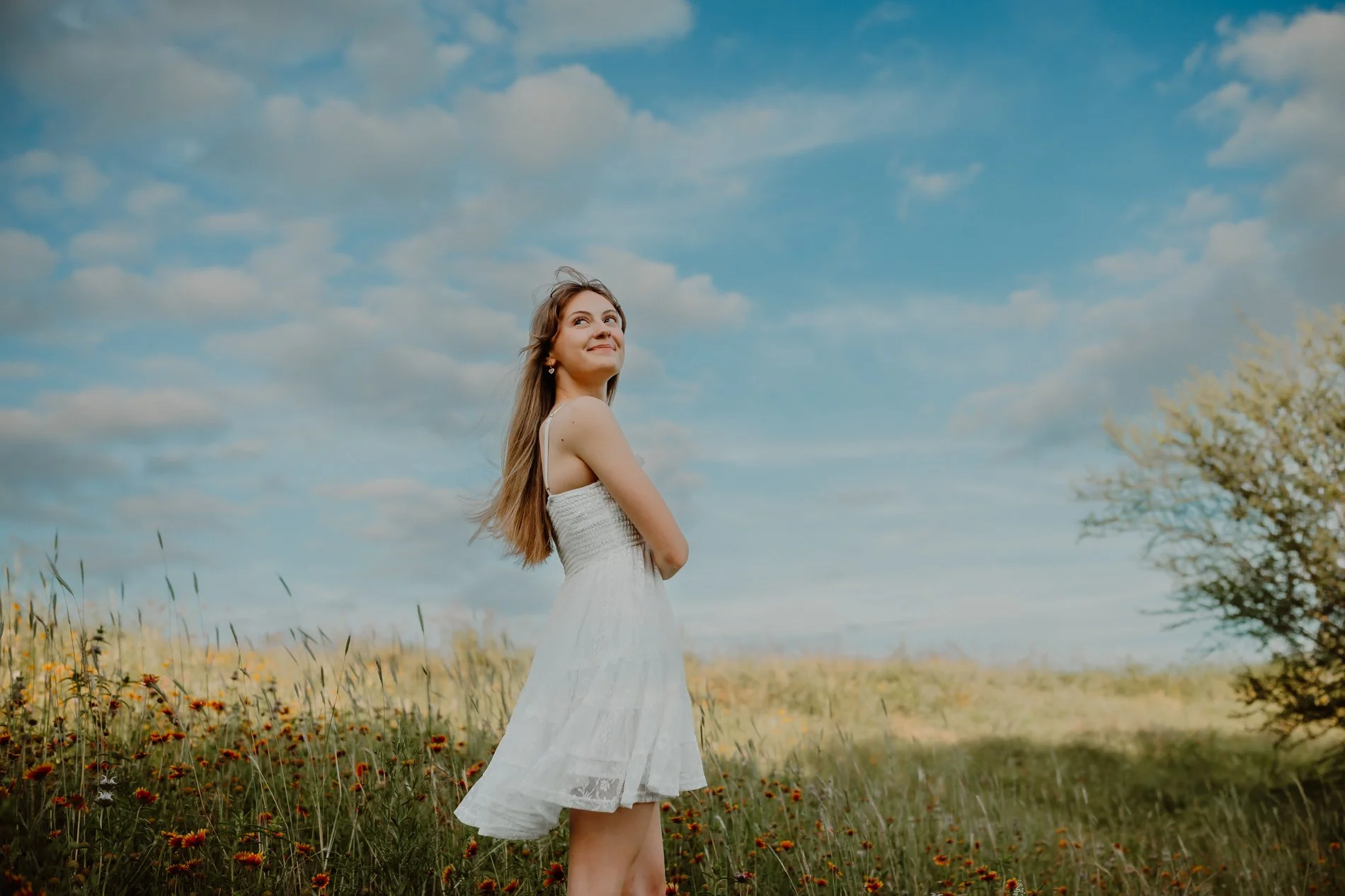 Natural-light senior session in the Austin wildflowers, featuring Dylann laughing in a sunlit meadow.