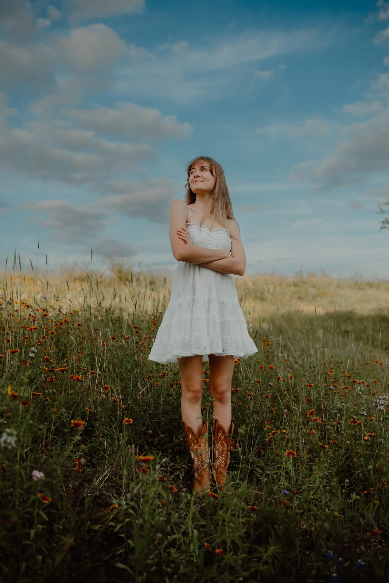 Class of 2026 senior girl standing among bluebonnets and wildflowers near Austin, Texas, photographed by lifestyle photographer.