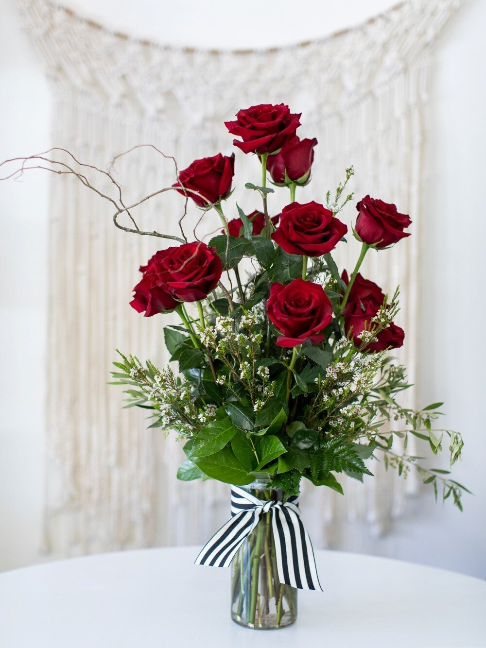 one dozen red roses arranged in glass vase accented with greenery and white blossoms