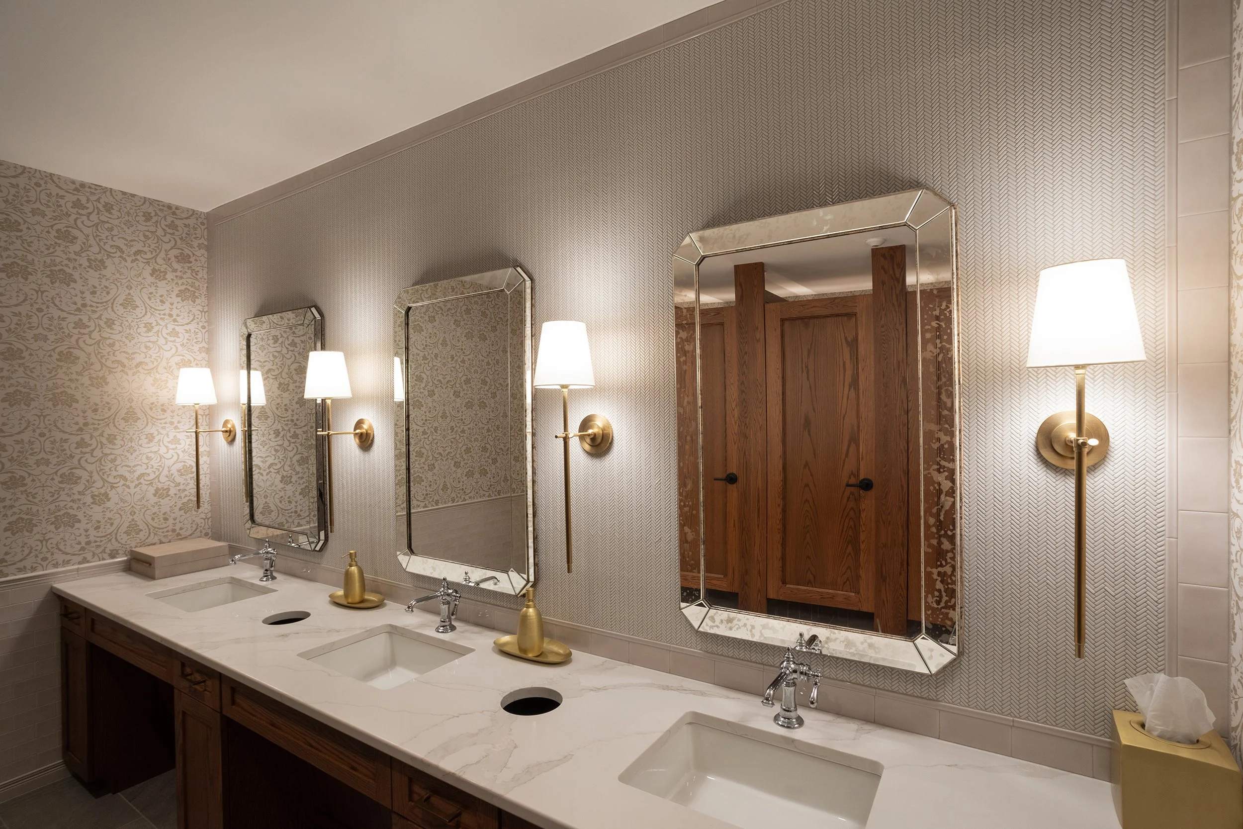 Bathroom with a double sink vanity, two mirrors, wall-mounted reading lamps, and a wooden door.