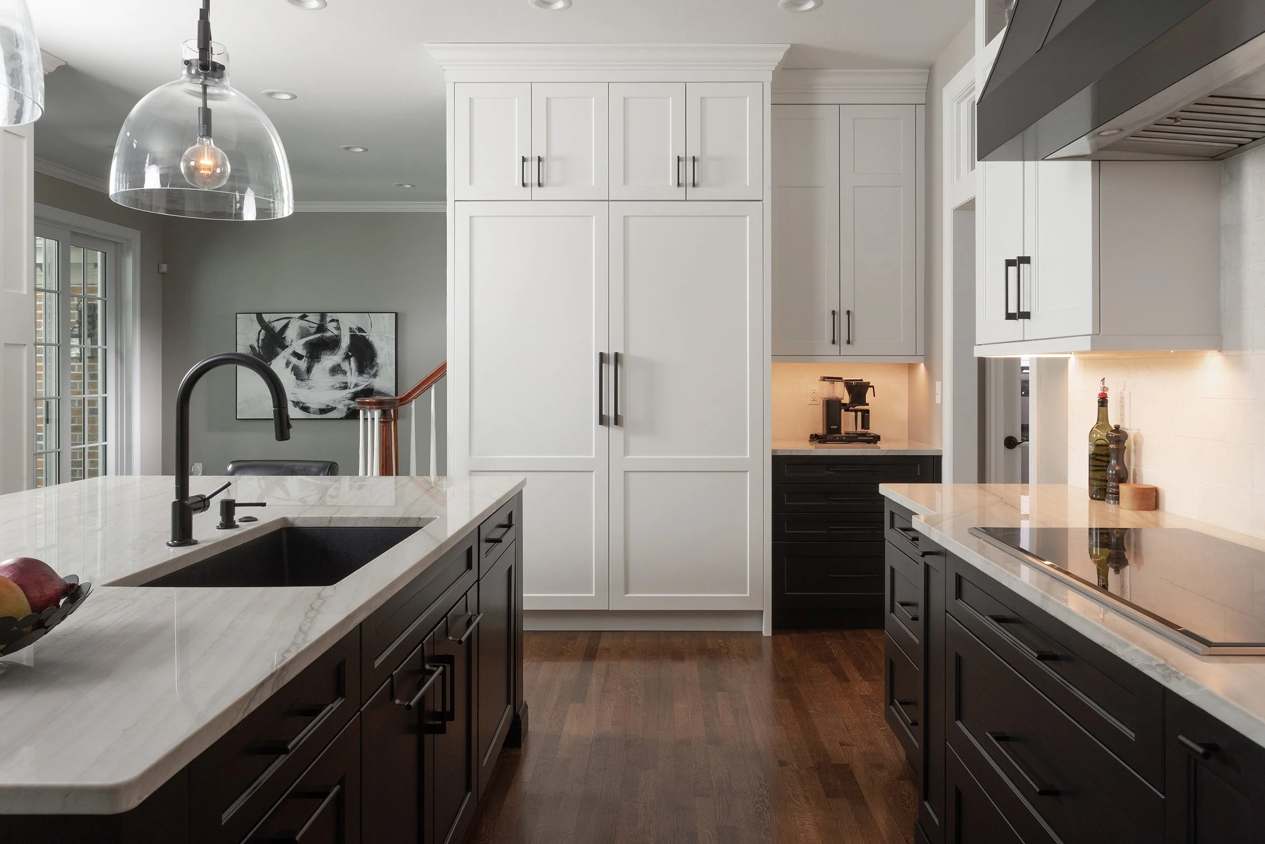 Modern kitchen with white cabinets, black lower cabinets, marble countertops, black faucet, and pendant lighting.