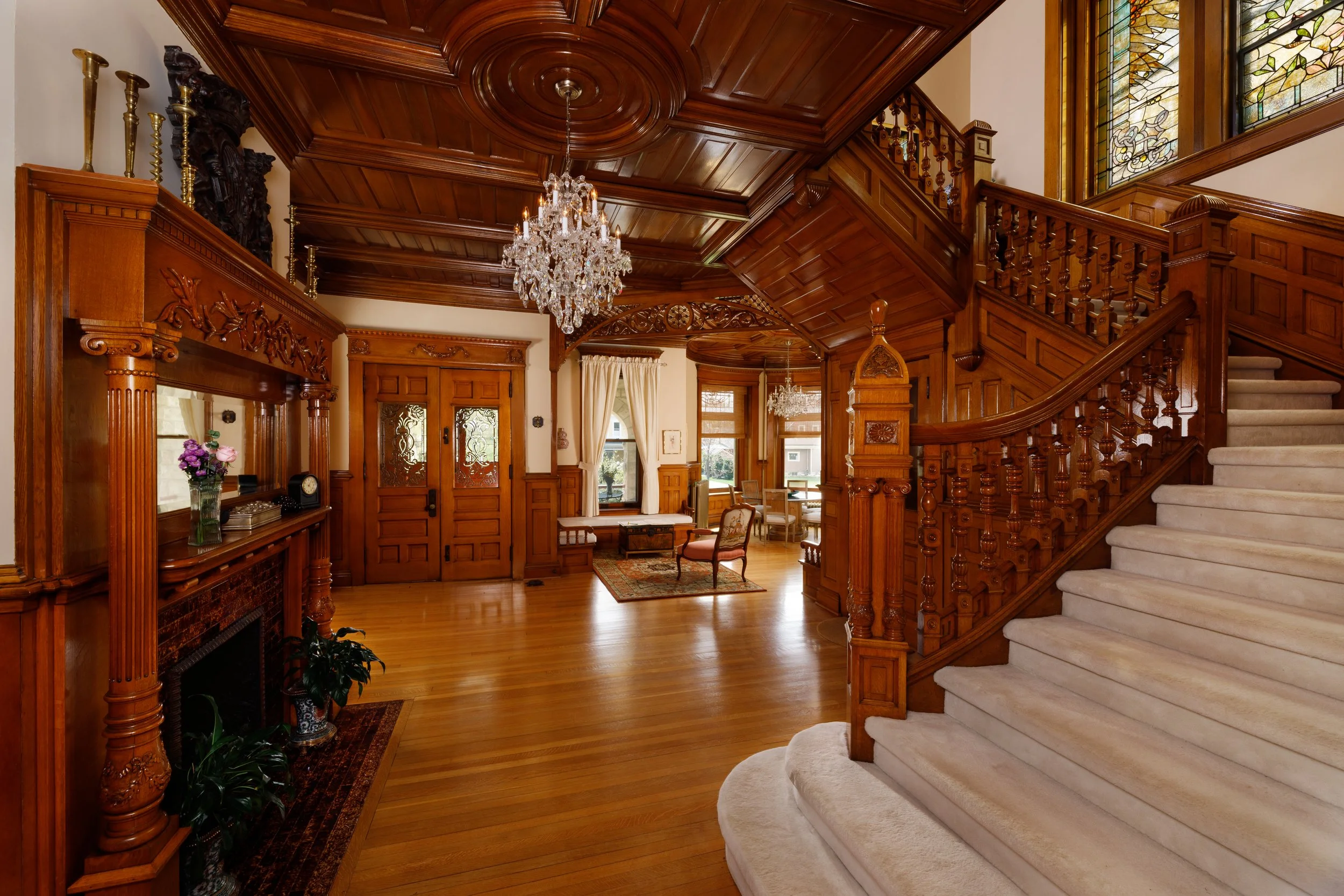 Interior of a historic home with wooden paneling, staircase, chandelier, and vintage furniture.