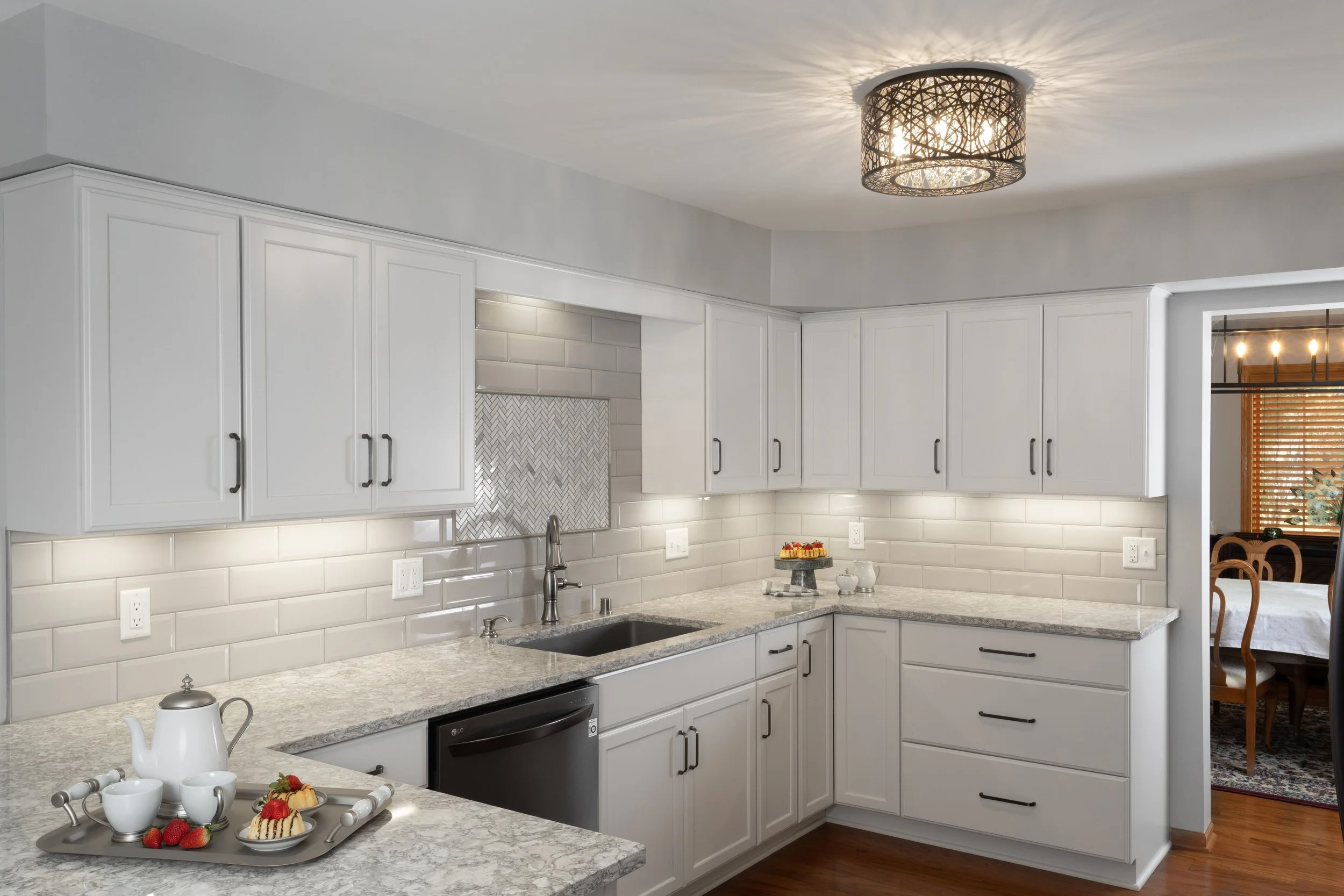 White kitchen with granite countertops, white cabinets, and a modern light fixture on the ceiling, with a view into a dining room.