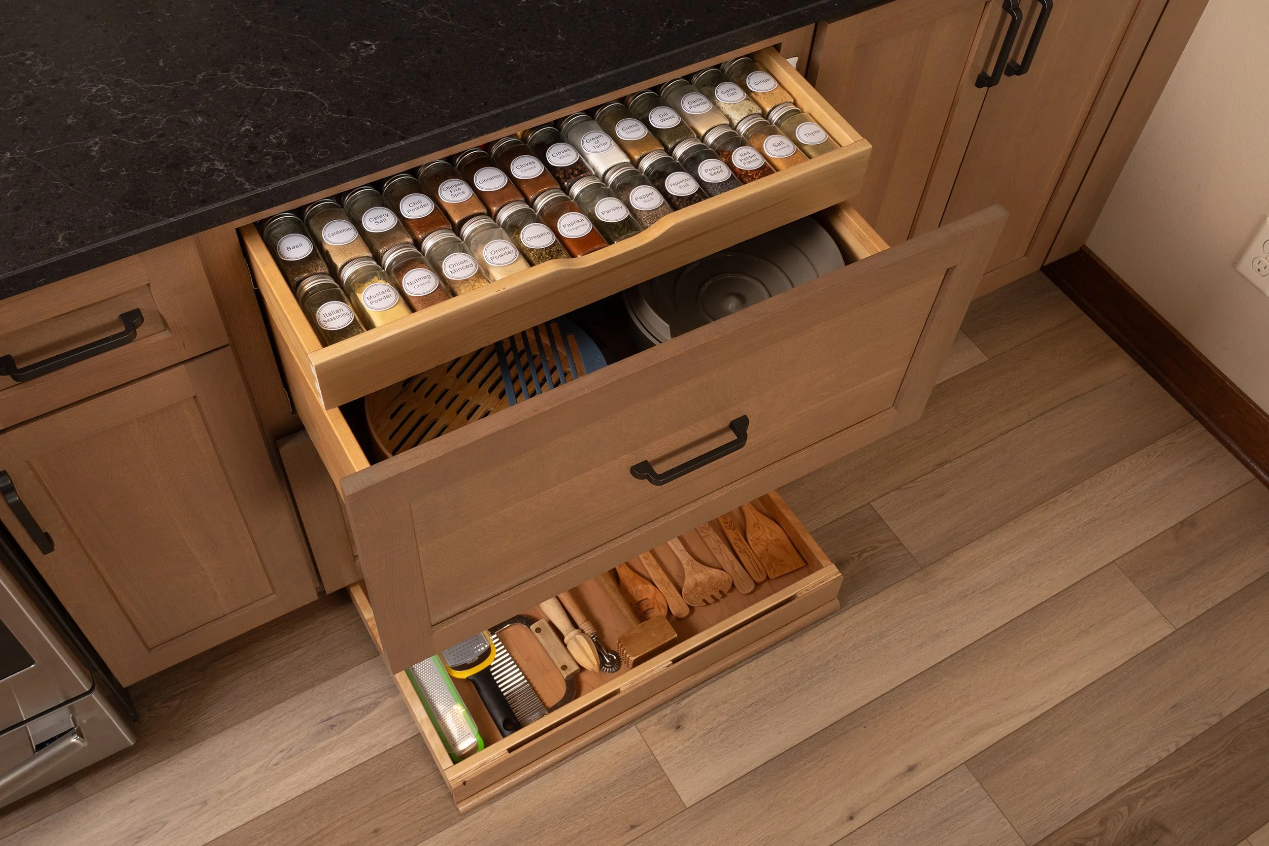 Kitchen drawer with spices in small jars, cooking utensils, and a grater inside