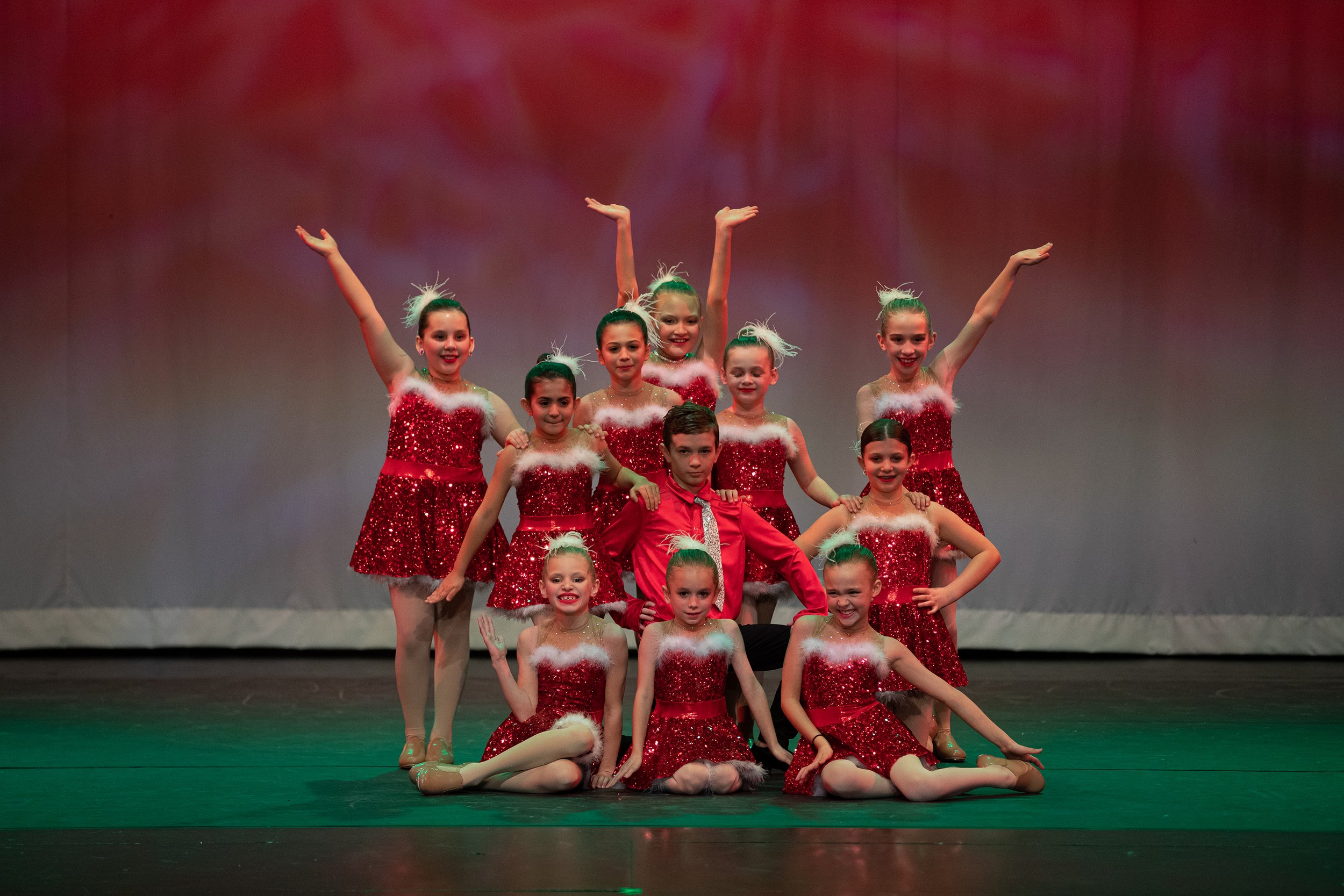 Group of young dancers dressed in red and white holiday-themed costumes, performing on stage in a dance recital.