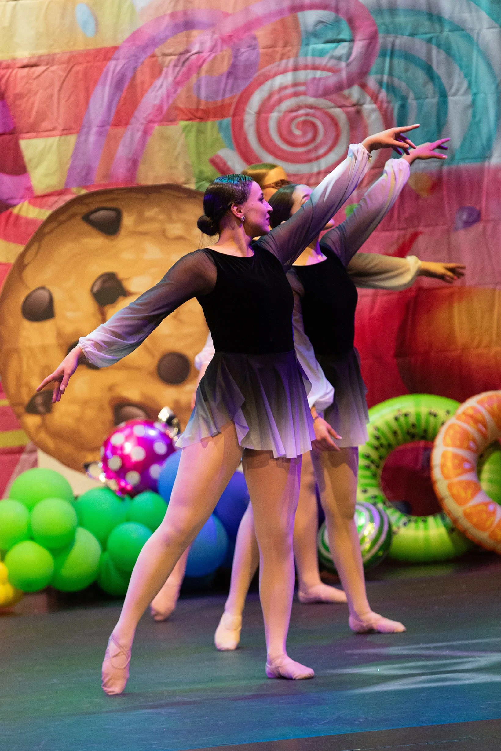 Ballet dancers performing on stage with a colorful backdrop featuring a large cookie and candy-themed decorations.