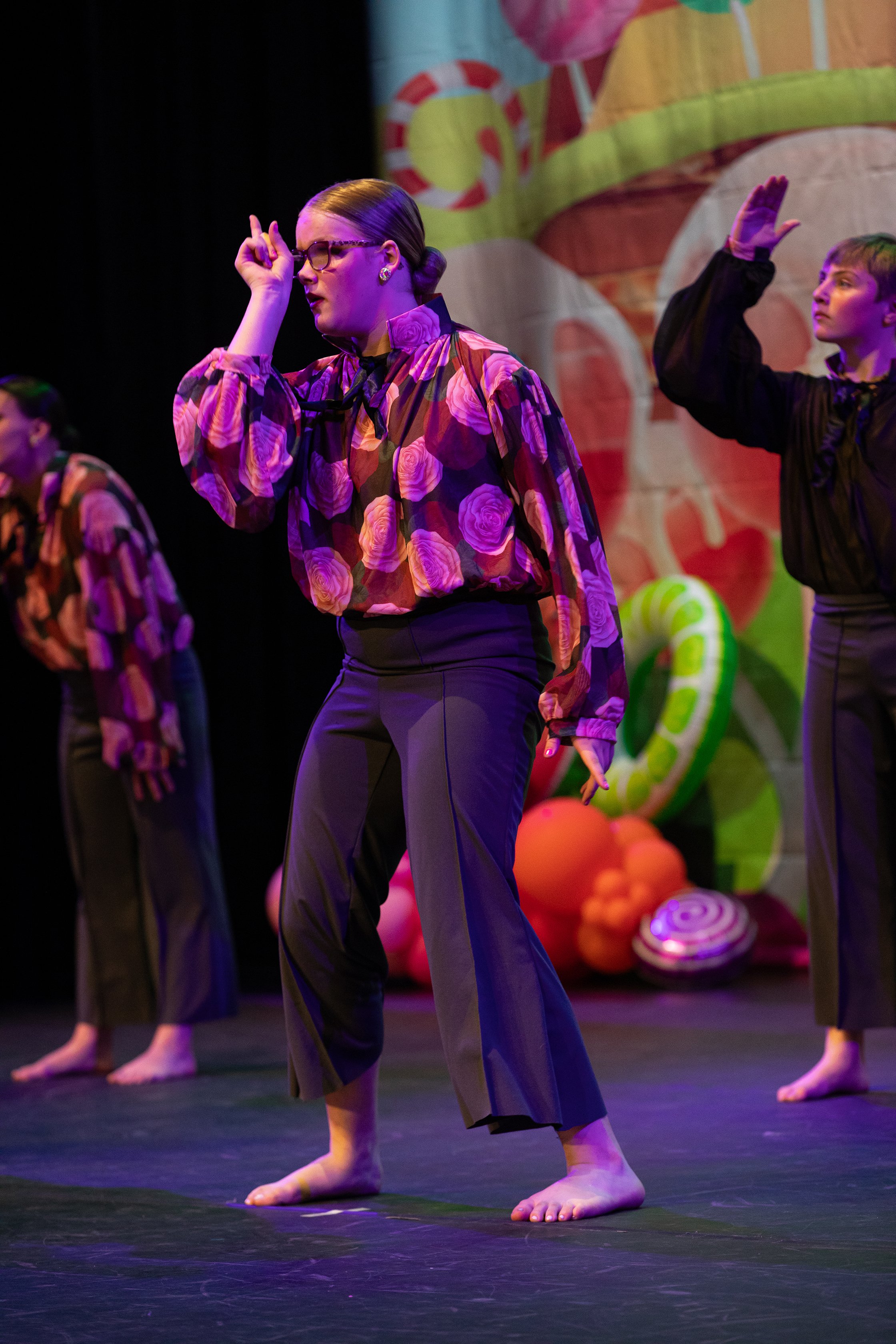 People performing a dance on stage with colorful candy-themed background.