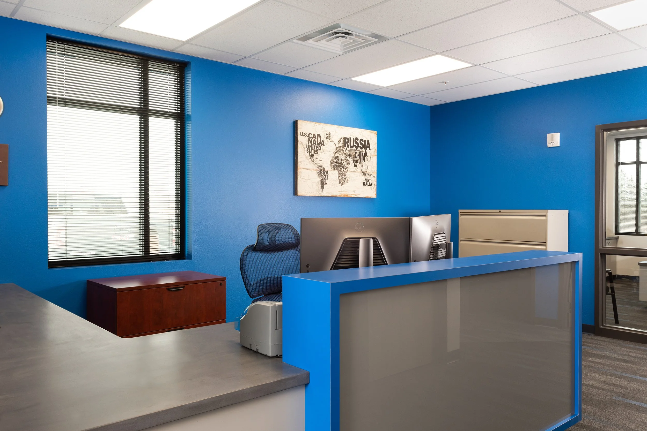 Interior view of an office with blue walls, a reception desk, a computer, and a world map artwork on the wall.