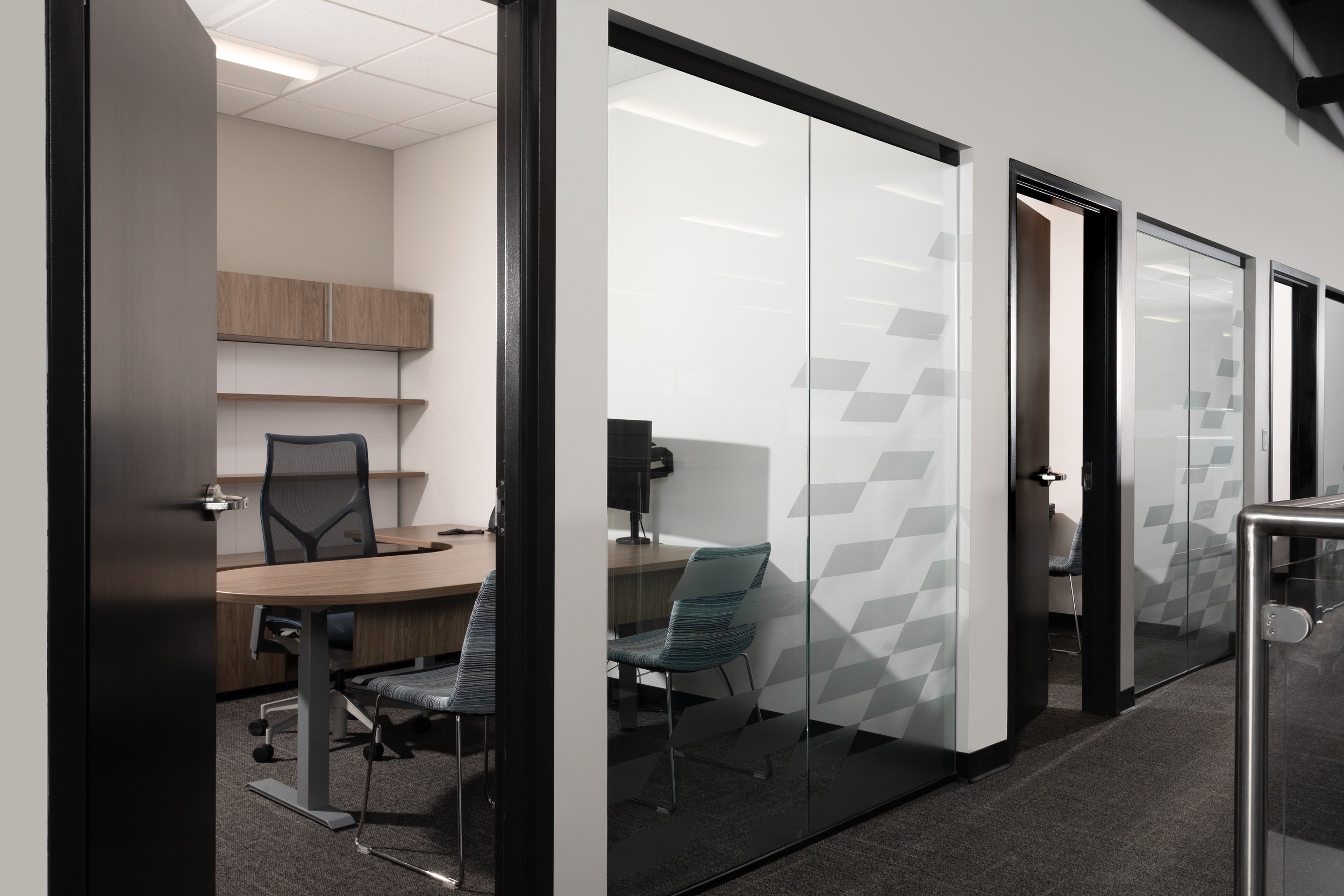 Modern office with glass-walled conference rooms and a black office chair behind a wood desk.
