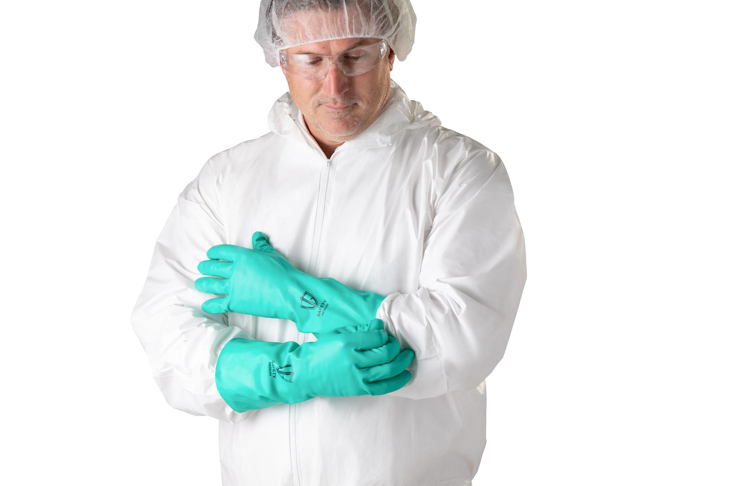 A person dressed in medical protective gear, including a white suit, a hair cap, goggles, and teal gloves, is adjusting the gloves with a focused expression.
