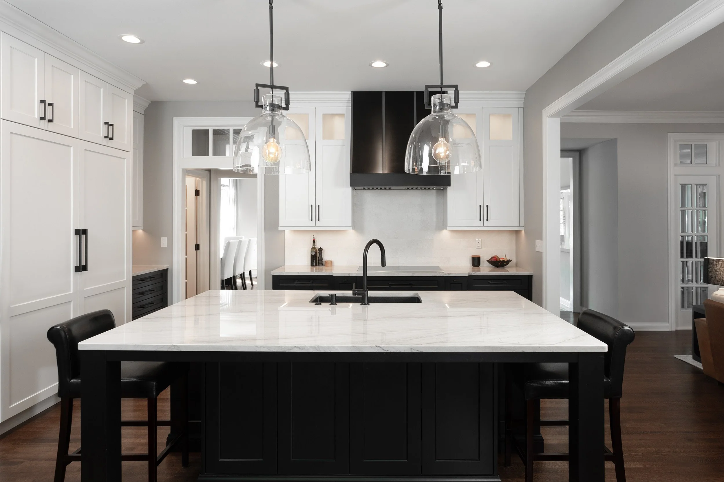 Modern kitchen with white cabinets, black accents, a large white island, and pendant lights hanging above.
