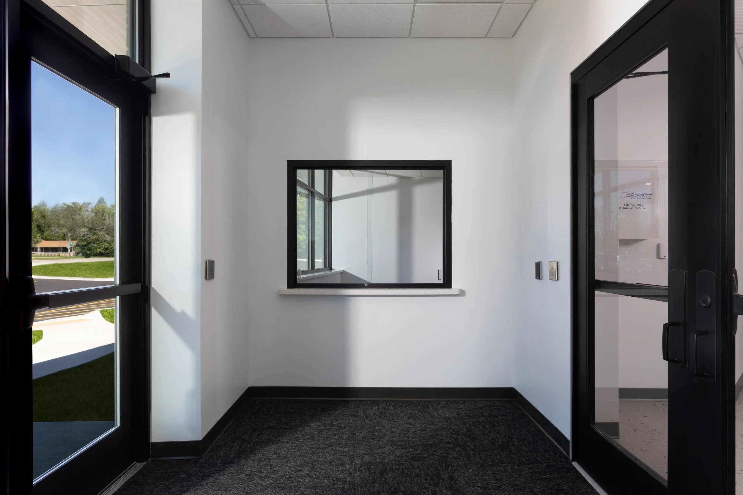 Empty room with white walls, black trim, a window in the wall, and glass door on the right in a modern building.