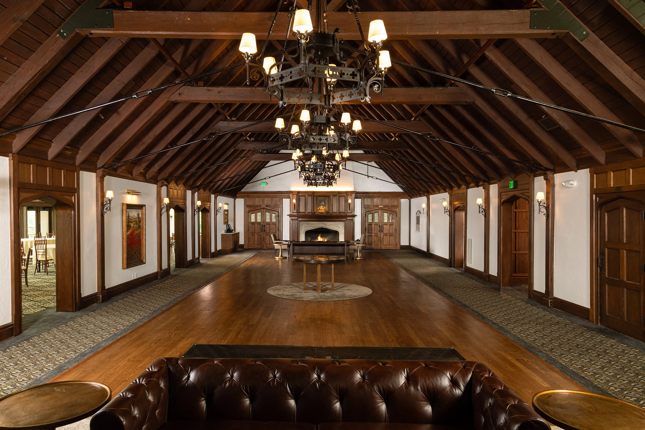 Elegant room with wooden vaulted ceiling, chandeliers, fireplace, and leather seating.