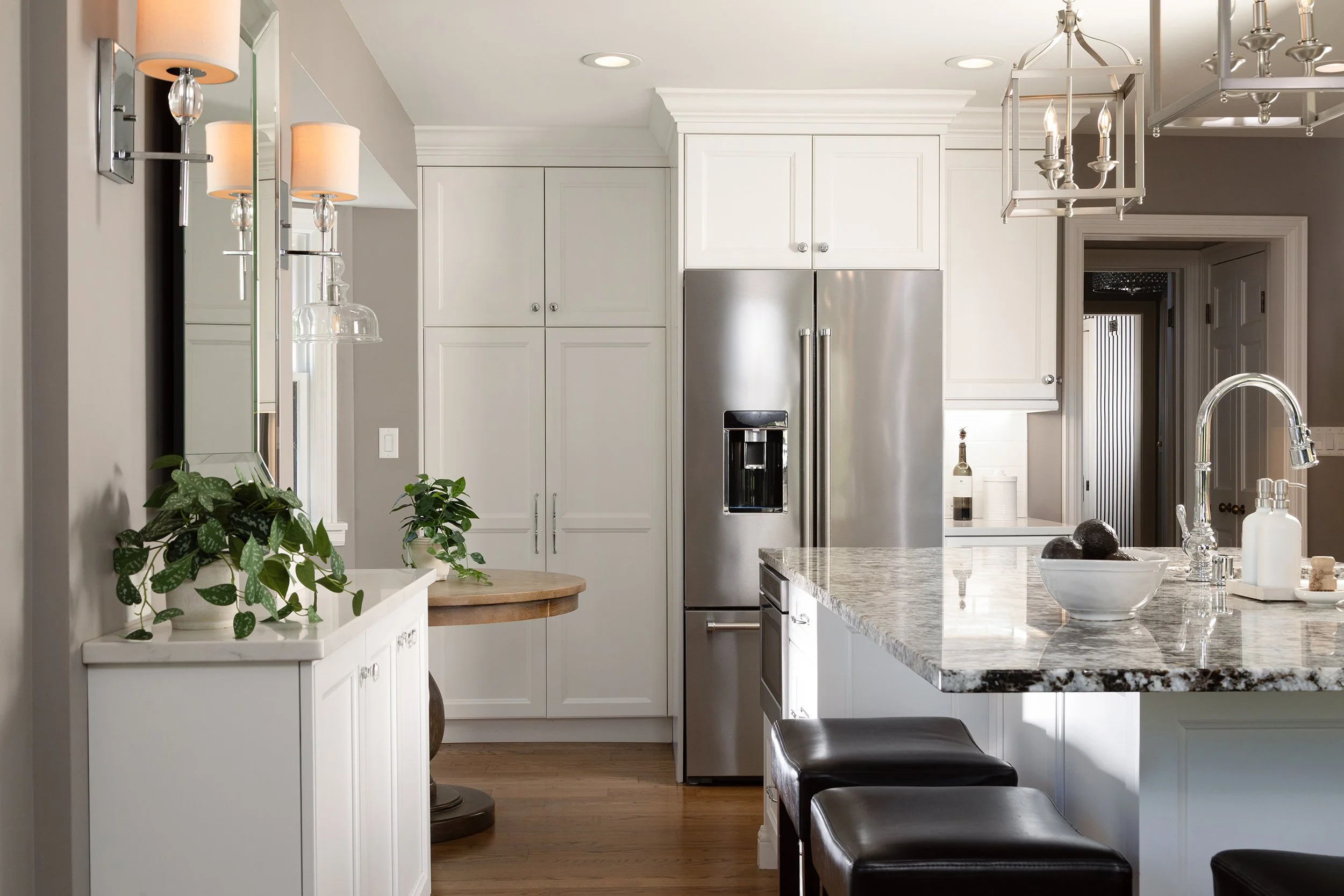 Modern kitchen with white cabinets, stainless steel refrigerator, granite countertops, pendant lights, and black leather stools.