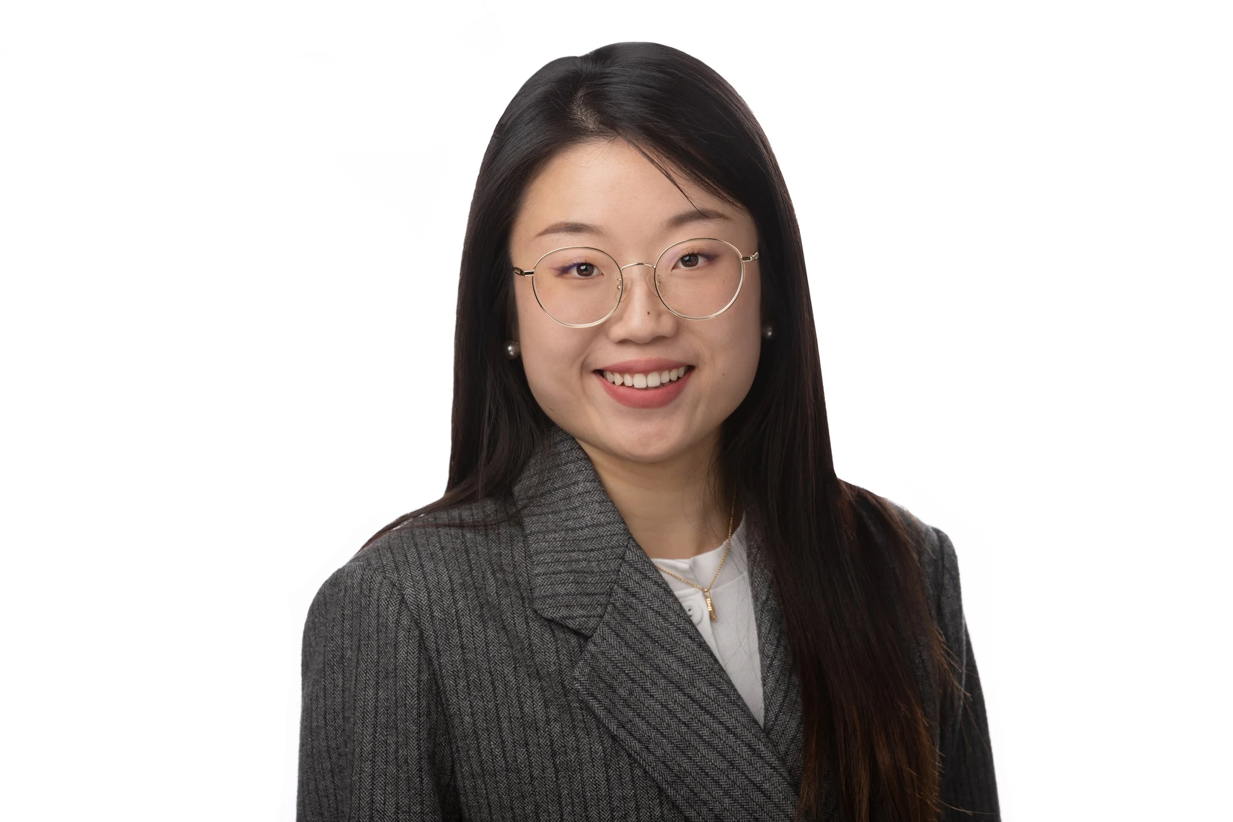 A portrait of a young Asian woman with long black hair, wearing glasses, pearl earrings, a gray pinstripe blazer, a white shirt, and a gold necklace, smiling against a white background.