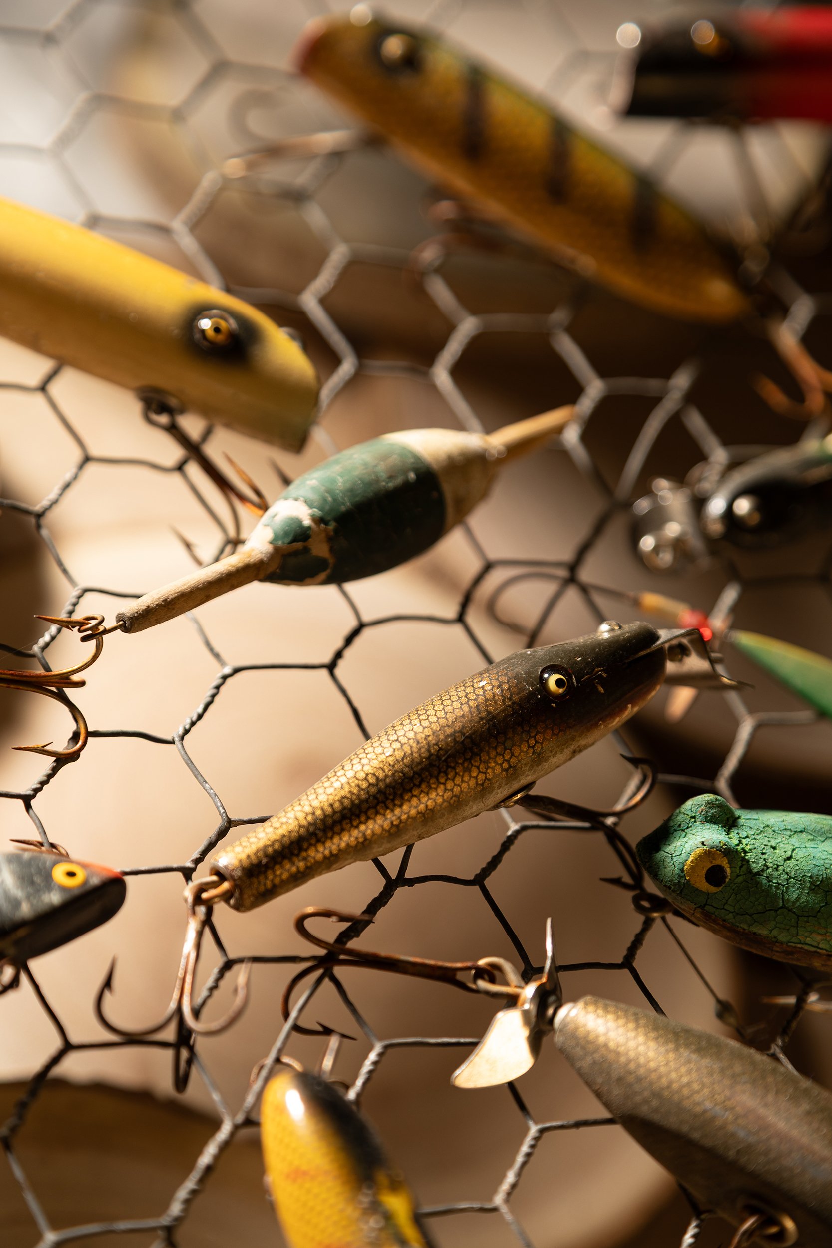 Close-up of various fishing lures hanging on a wire mesh display.