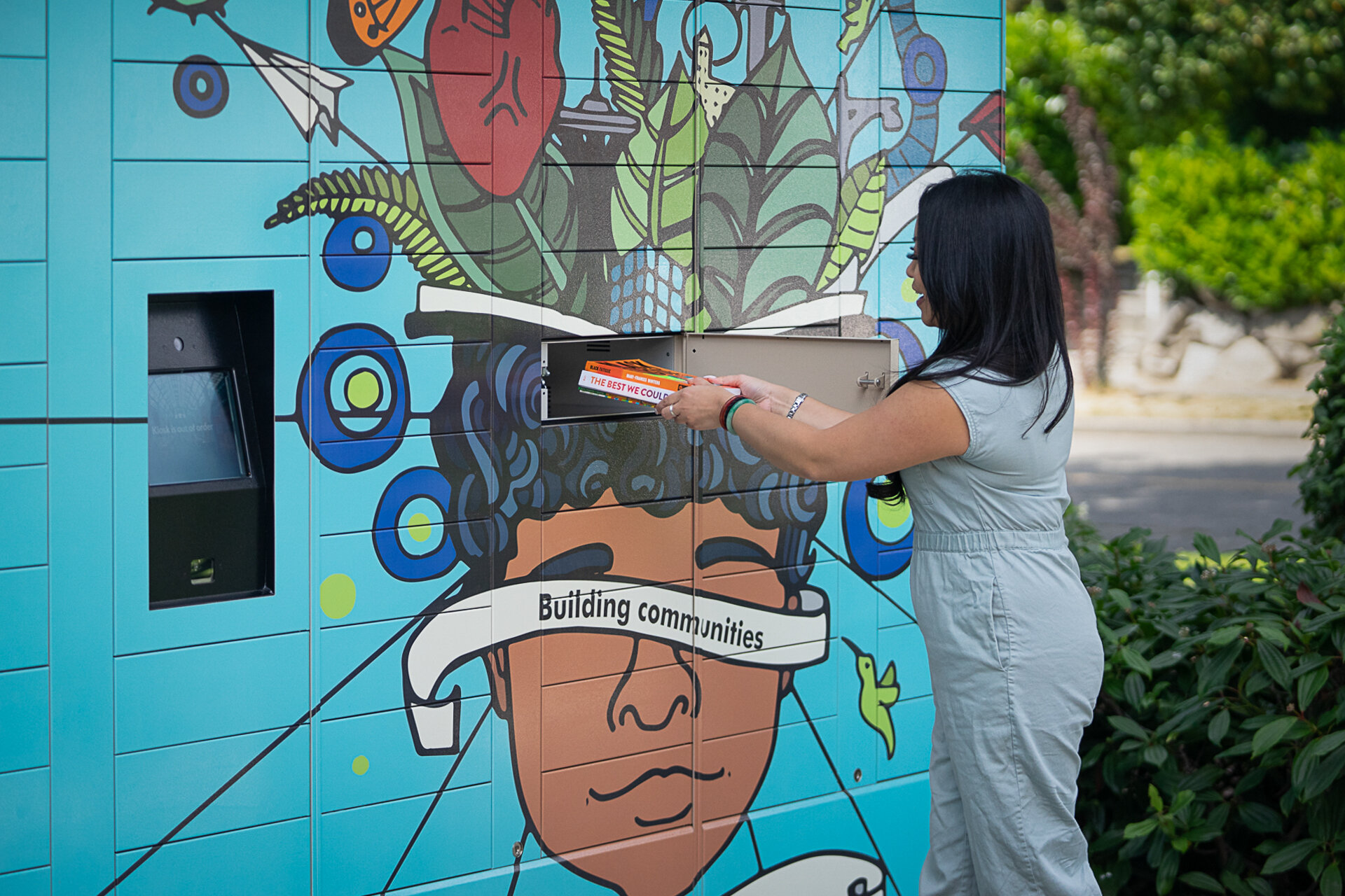  A Seattle library staff member demonstrates the new library locker system with art by local artist Carlos Martinez.  
